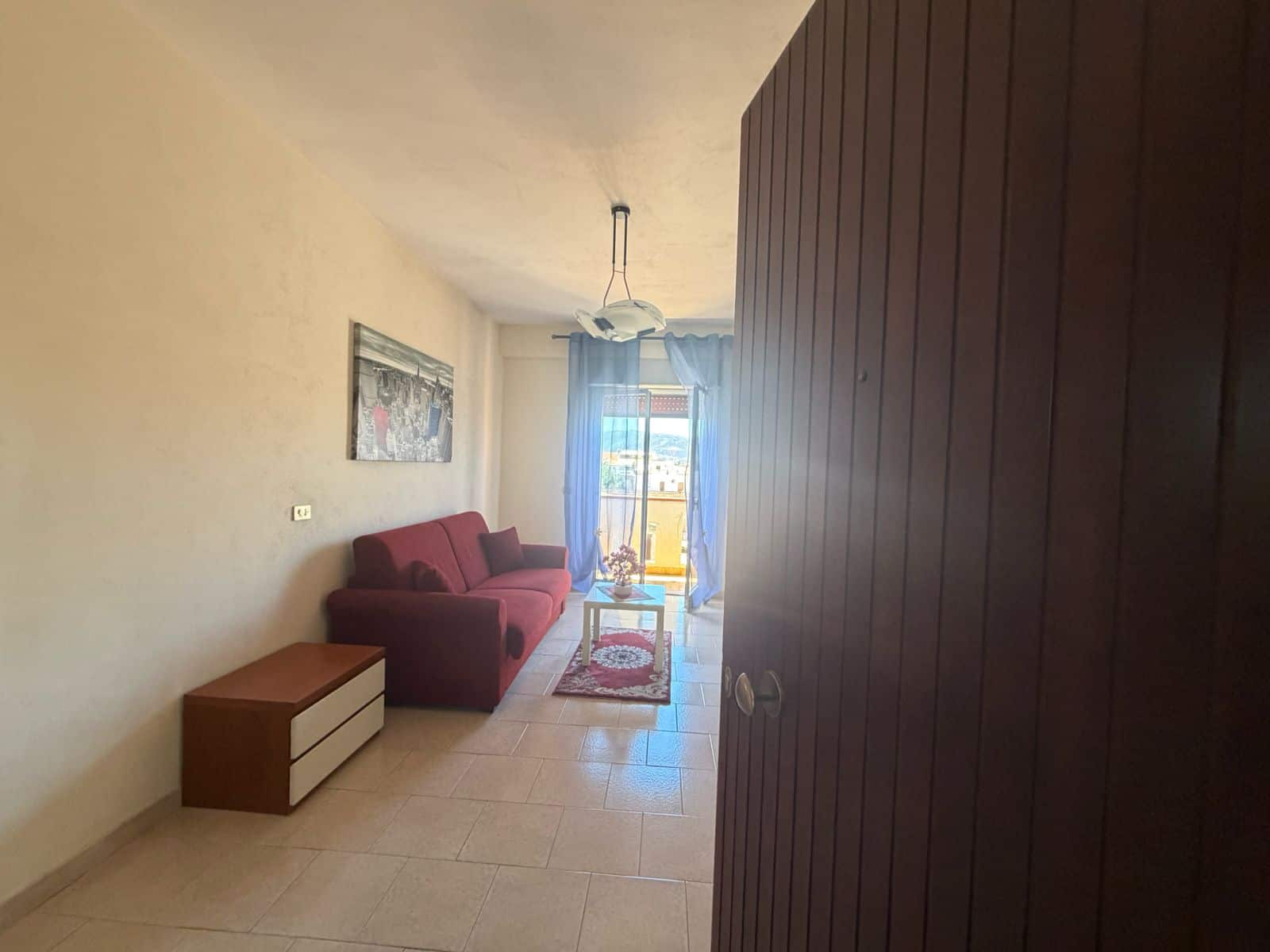 Interno di un appartamento con divano rosso, tavolino e balcone con vista mare a Terme Vigliatore.