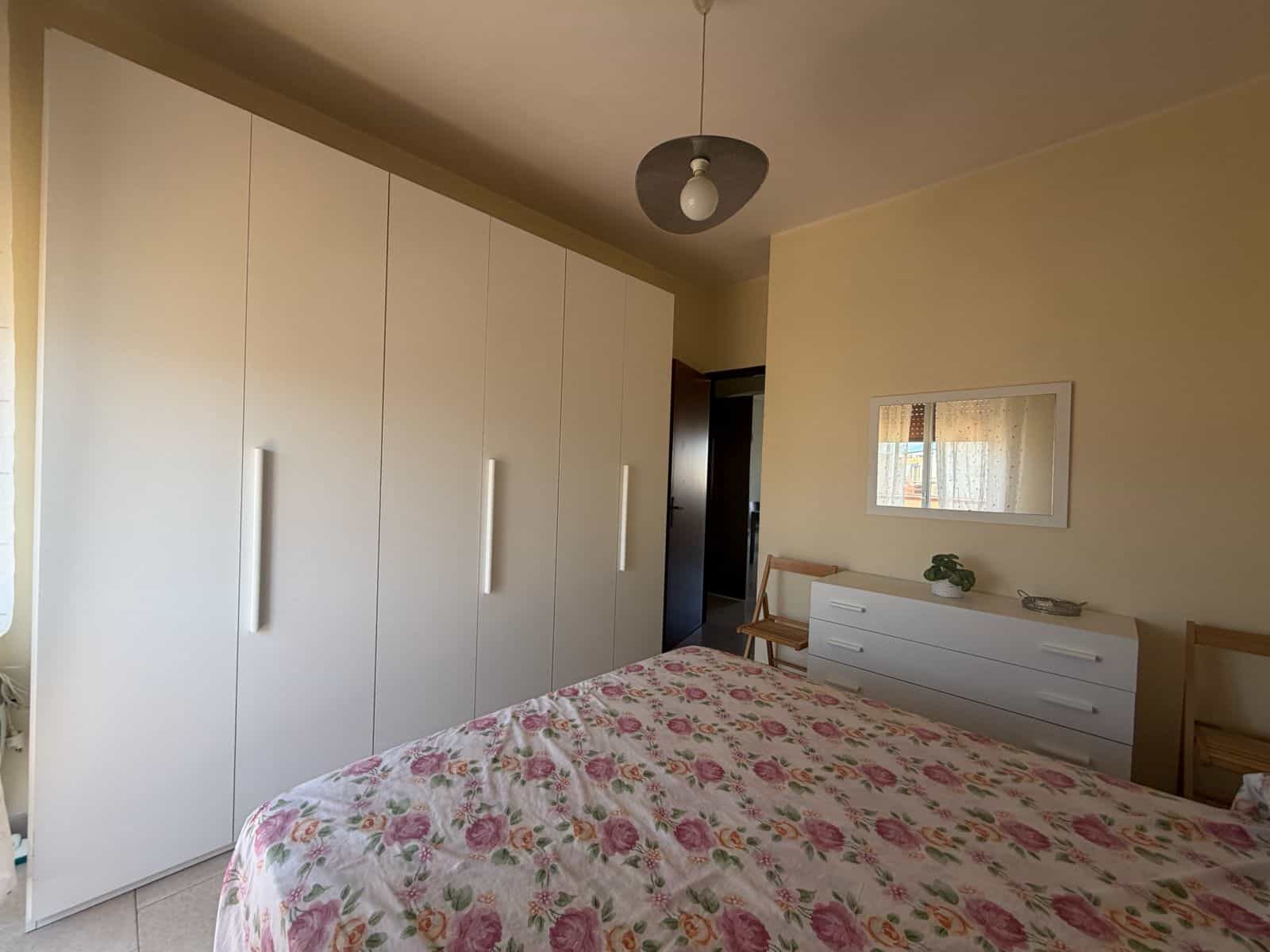 Camera rivolta verso una camera da letto con armadio bianco e letto con copriletto floreale rosa e verde.