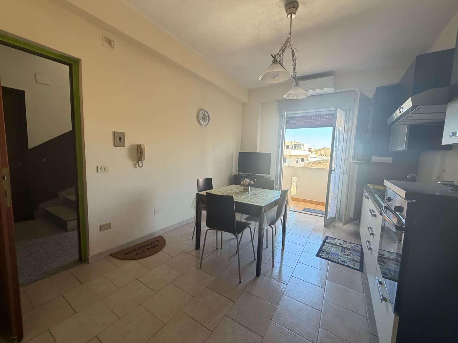 Interno di un appartamento con cucina e zona pranzo, vista su balcone con vista panoramica.