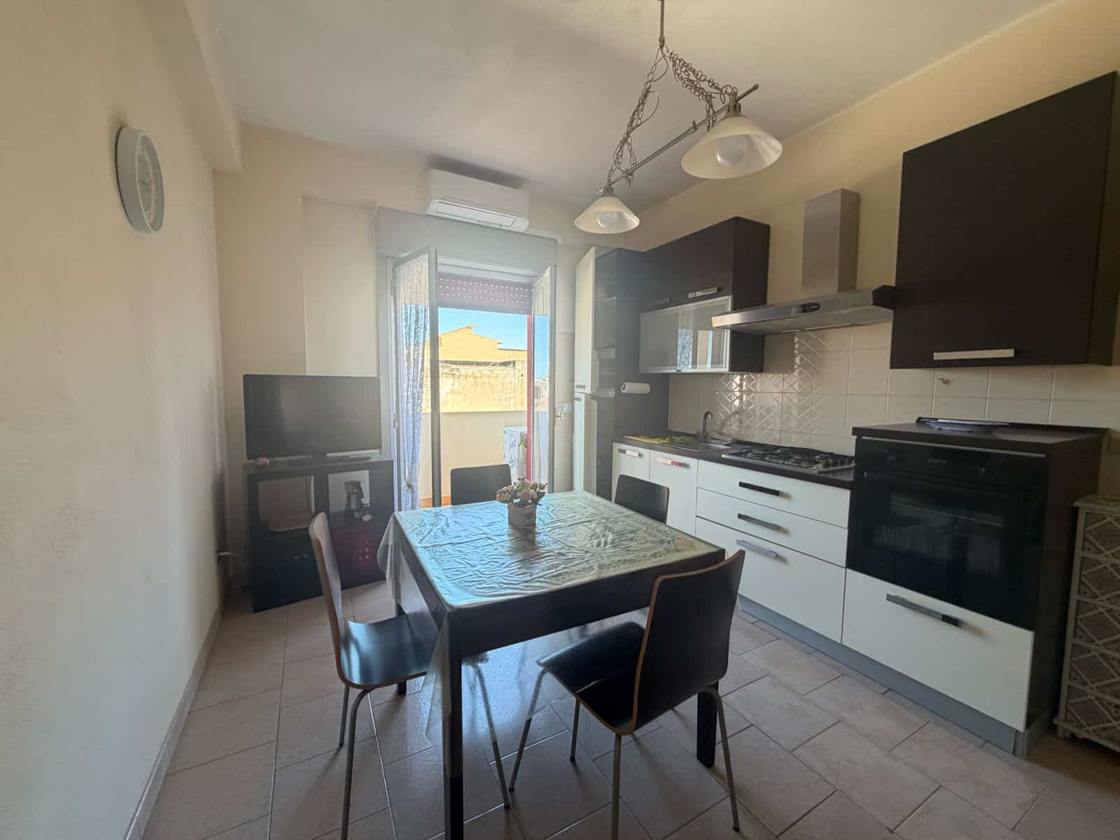 Cucina moderna con mobili neri e bianchi, tavolo con sedie e accessori, luce naturale dalla finestra.