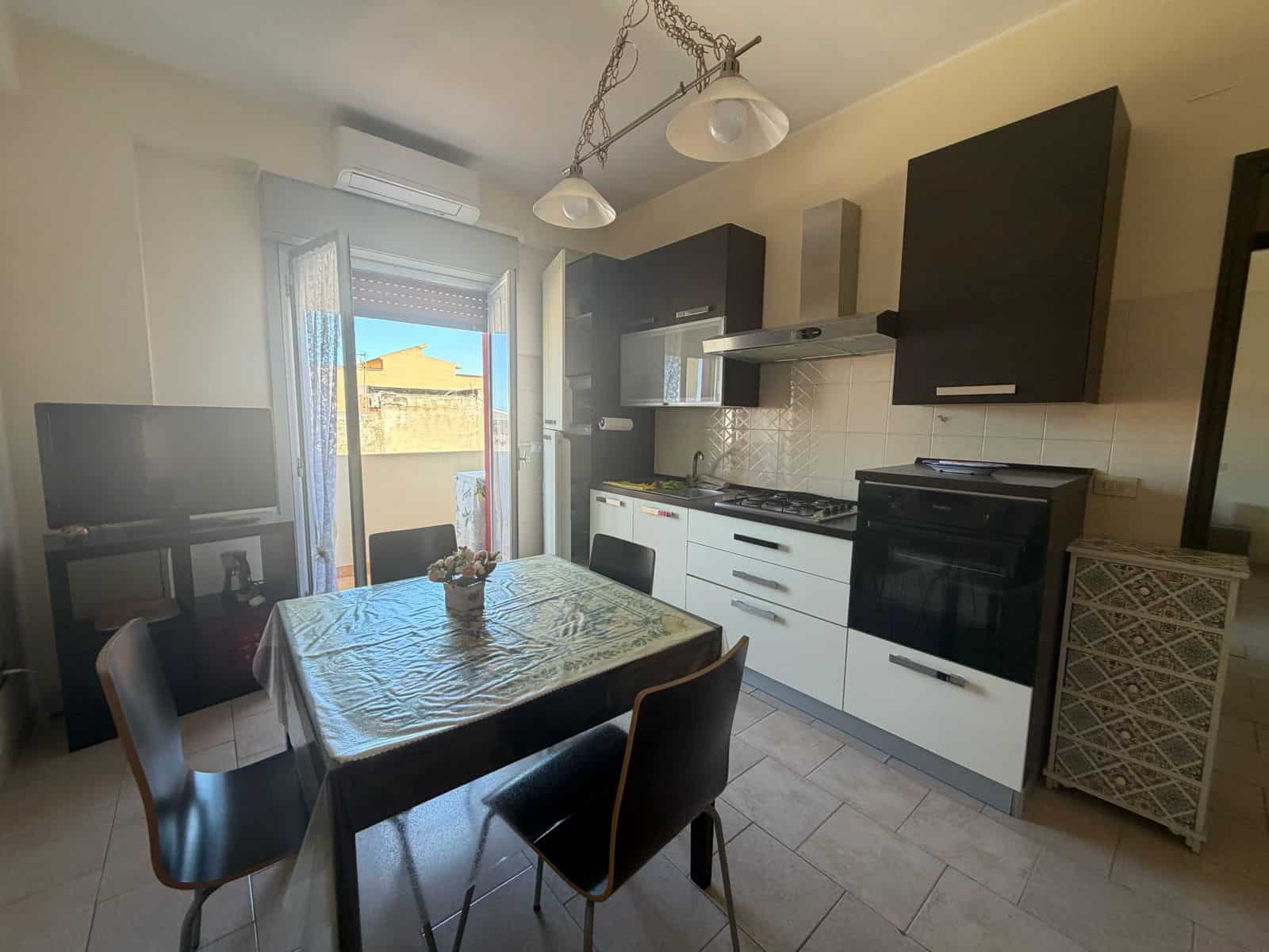 Cucina moderna in appartamento a Terme Vigliatore con mobili neri e bianchi, tavolo con tovaglia e vista sulla terrazza esterna.