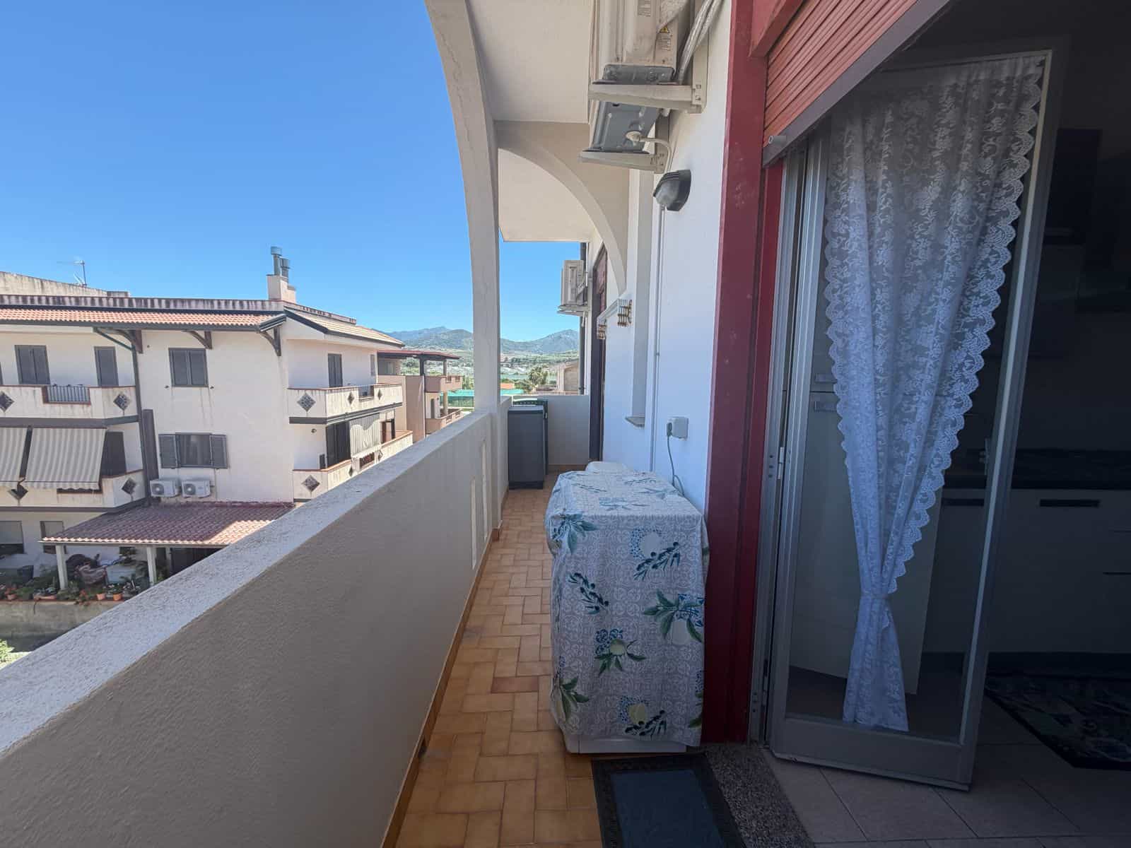 Balcone di un appartamento con vista sulle case di Terme Vigliatore, in Sicilia, con aria condizionata e porta finestra aperta.