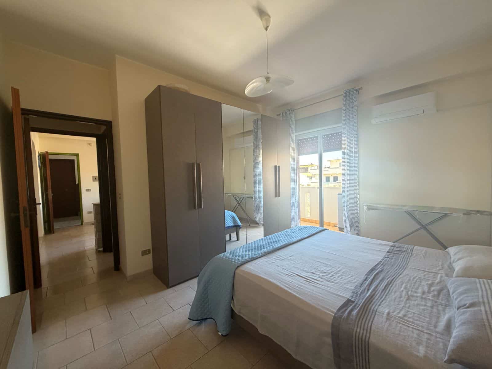 Camera da letto luminosa con letto matrimoniale, armadio e balcone con vista sulla città, in appartamento a Terme Vigliatore.