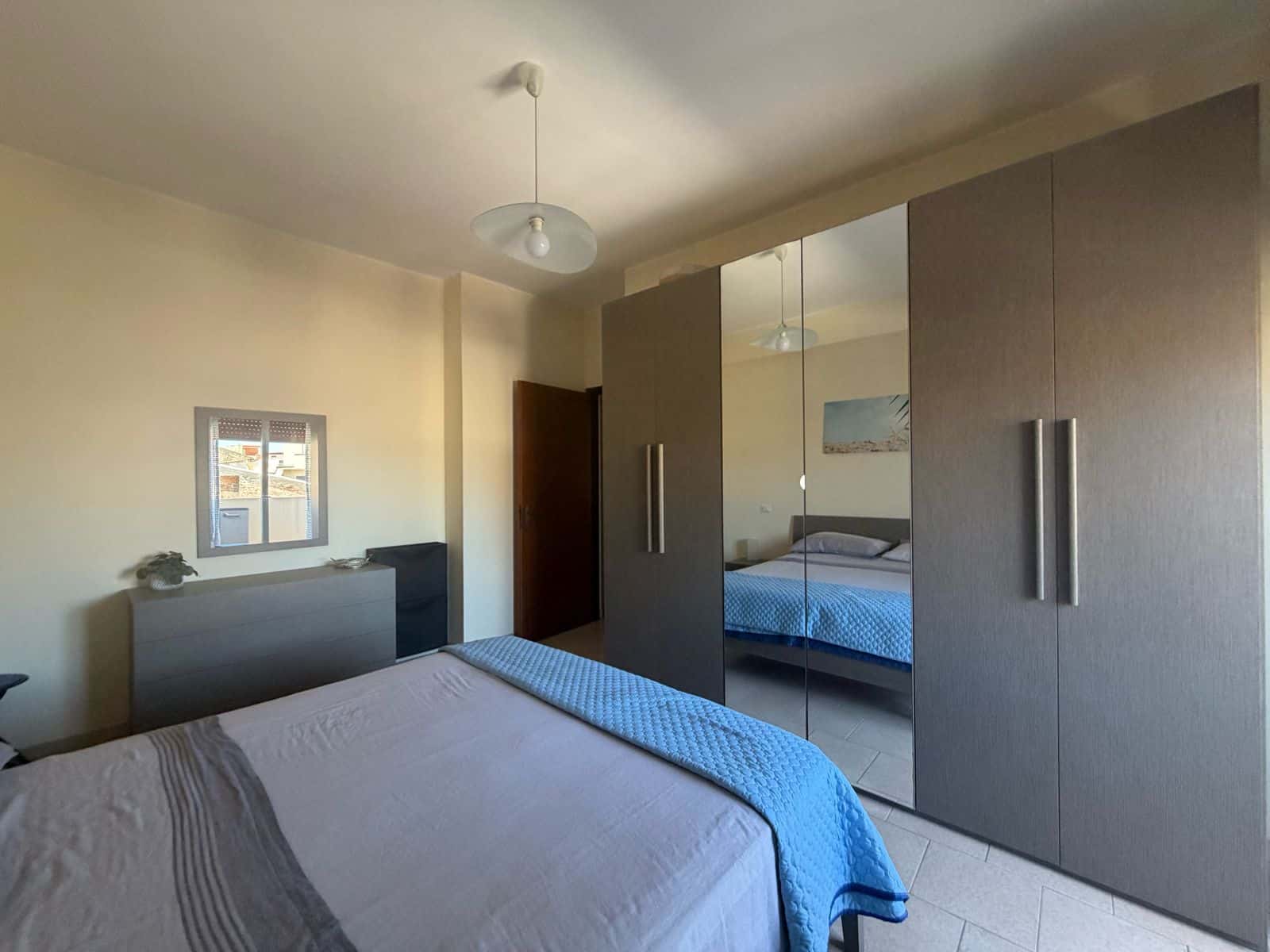 Camera da letto moderna con armadio a specchio e finestra, ambiente luminoso e accogliente.