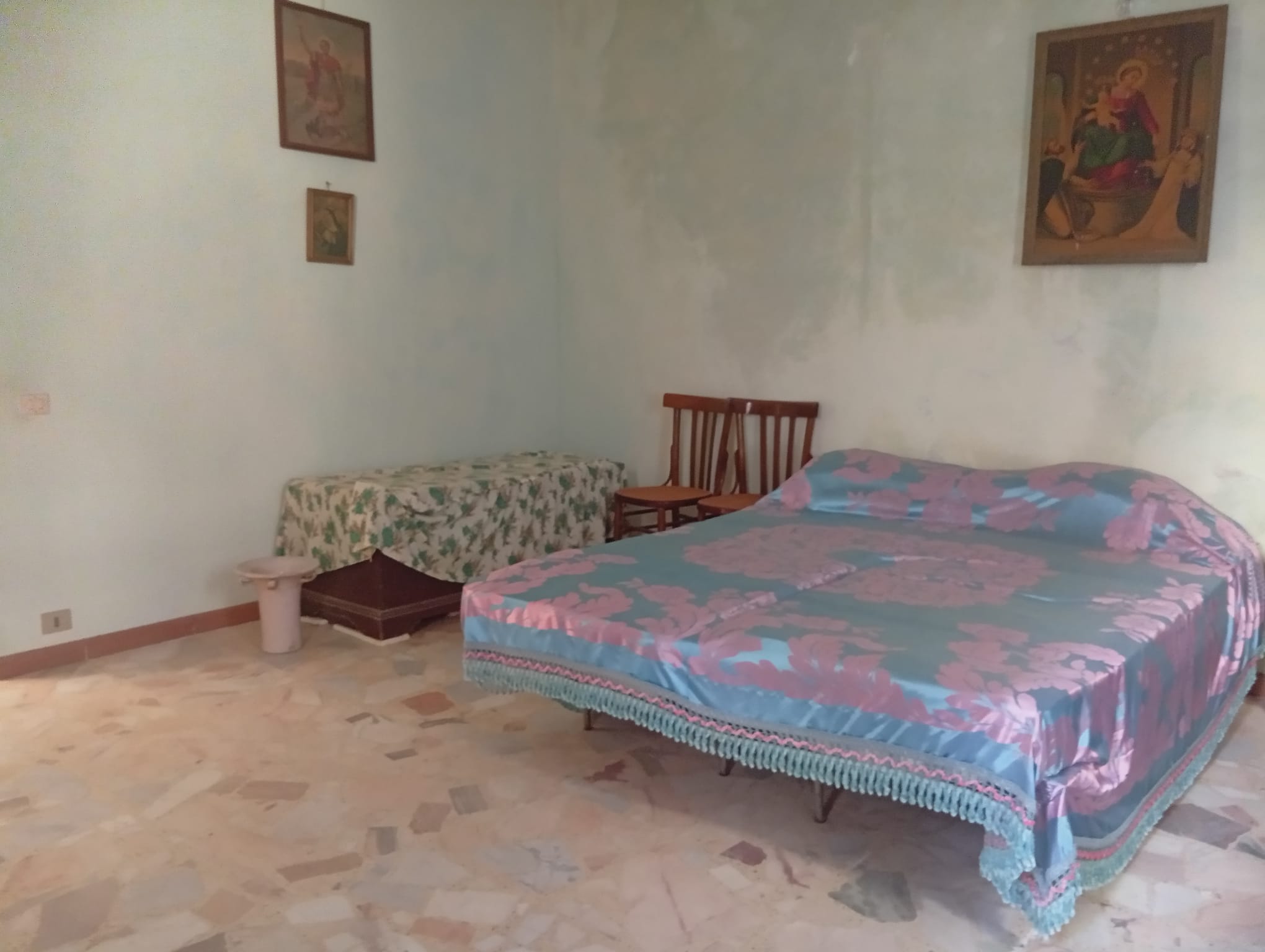 Camera che mostra una camera da letto semplice con letto matrimoniale, sedie e quadri alle pareti.