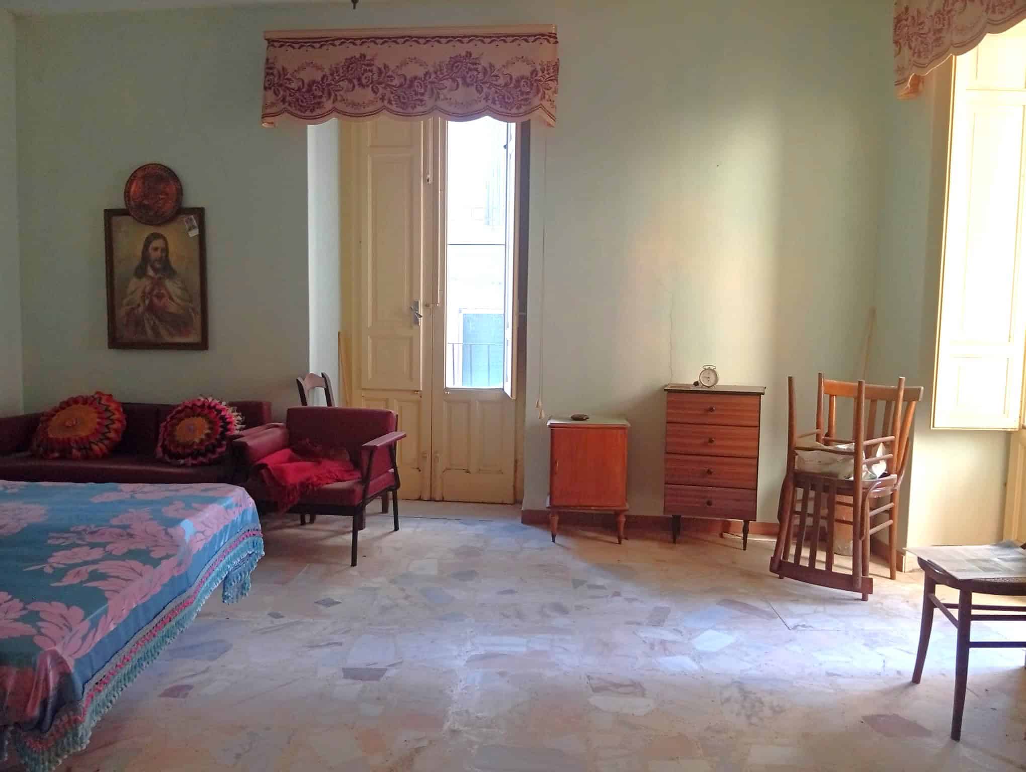 Interno di una casa semidipendente con pareti verdi, mobili d'epoca e grandi finestre che lasciano entrare molta luce naturale.