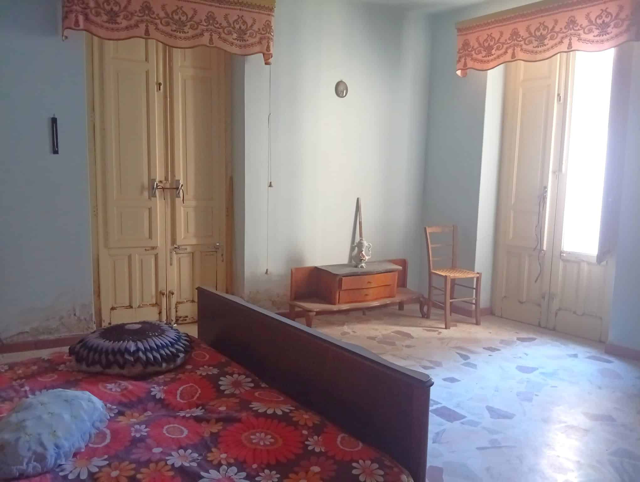 Camera che mostra una camera da letto con pareti azzurre, un letto con copriletto floreale rosso, e mobili d'epoca in legno chiaro.