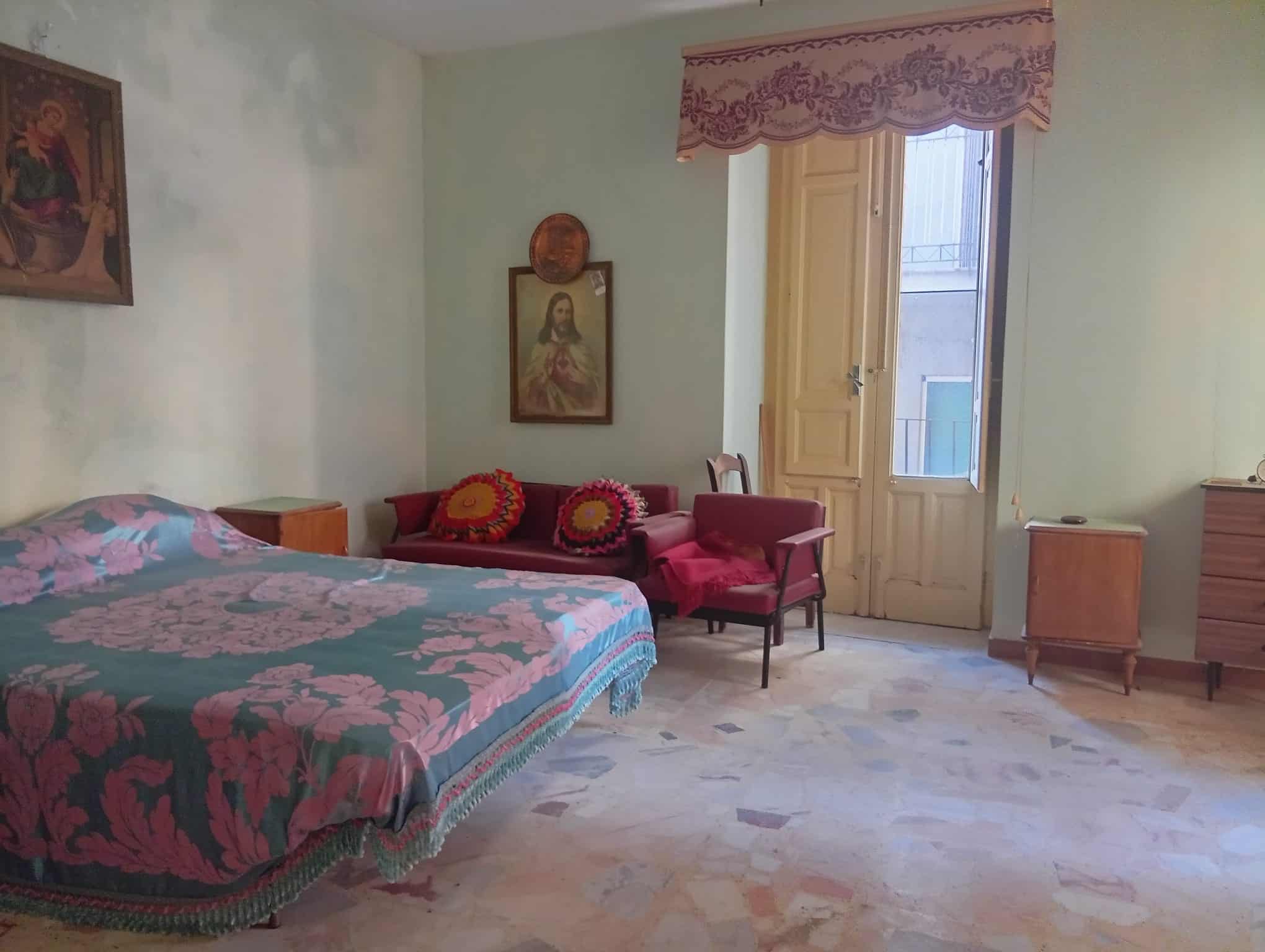 Camera da letto spaziosa con letto matrimoniale, divano, e balcone con vista su strada in una casa in vendita a Ficarra, Messina.
