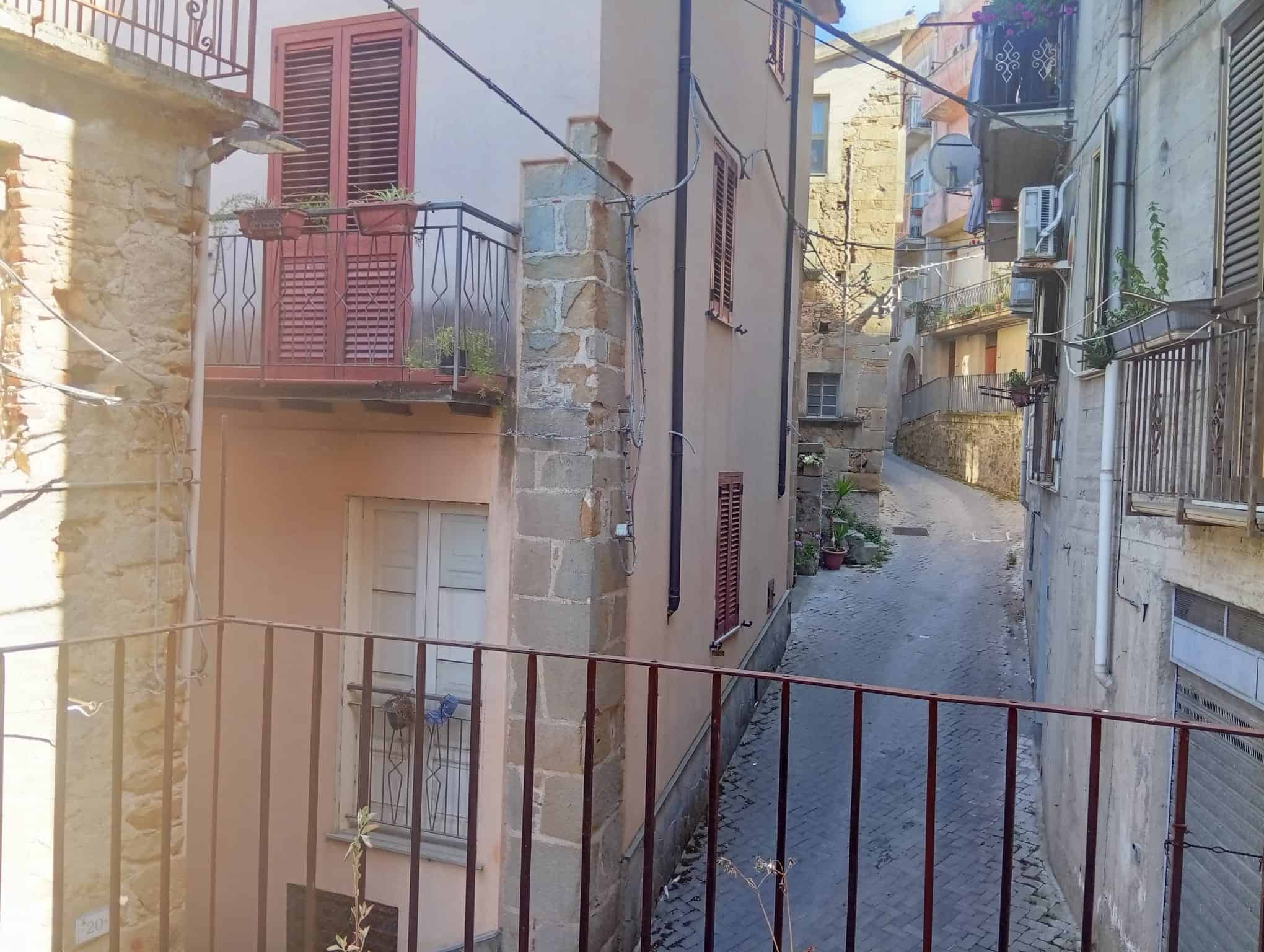 Vista di un vicolo stretto e caratteristico a Ficarra, con edifici storici e balconi in ferro battuto.