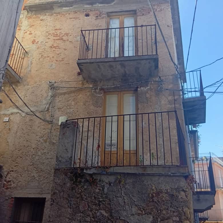 Facciata di una casa semidipendente in vendita a Ficarra, con balconi e pareti in pietra e intonaco.