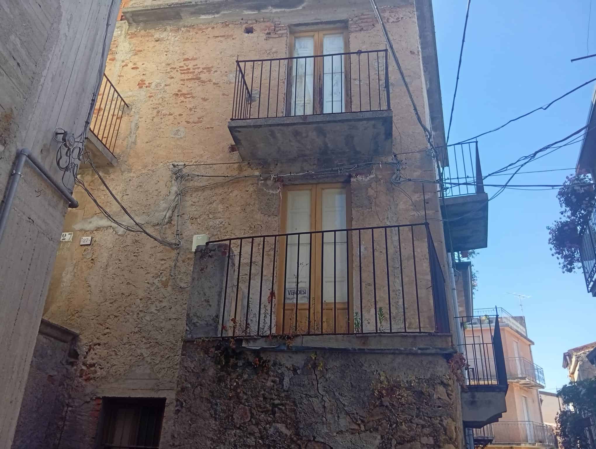 Facciata di una casa semidipendente in vendita a Ficarra, con balconi e pareti in pietra e intonaco.