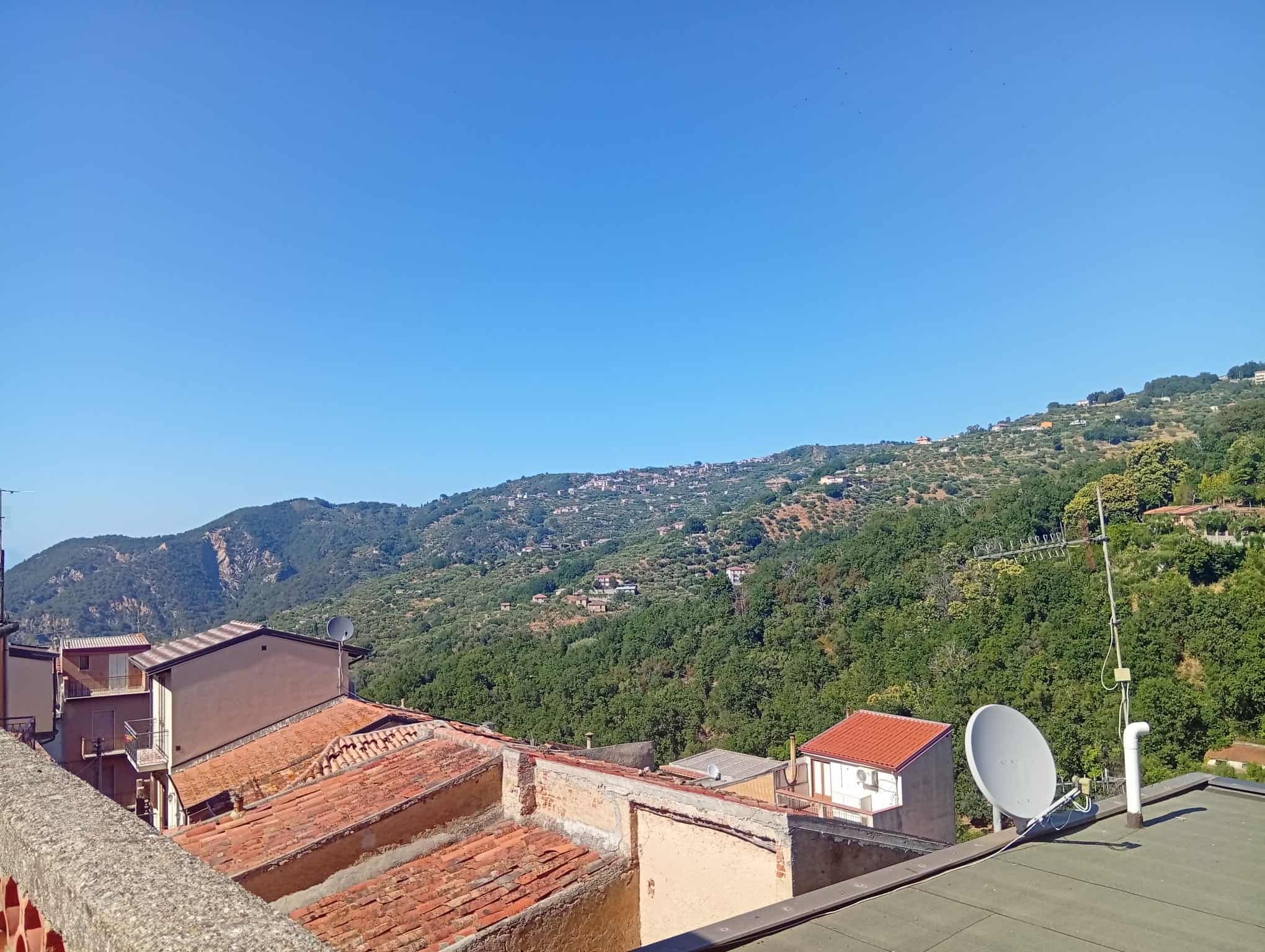 Vista panoramica delle case e delle colline verdi di Ficarra con cielo sereno.