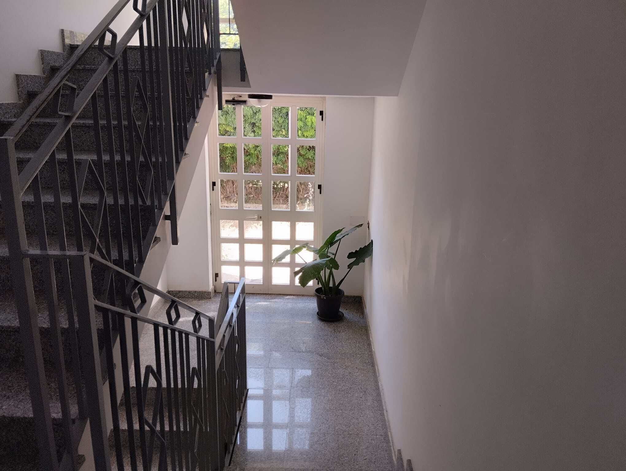 Ingresso condominiale con scala e porta vetrata, ambiente luminoso e pulito.