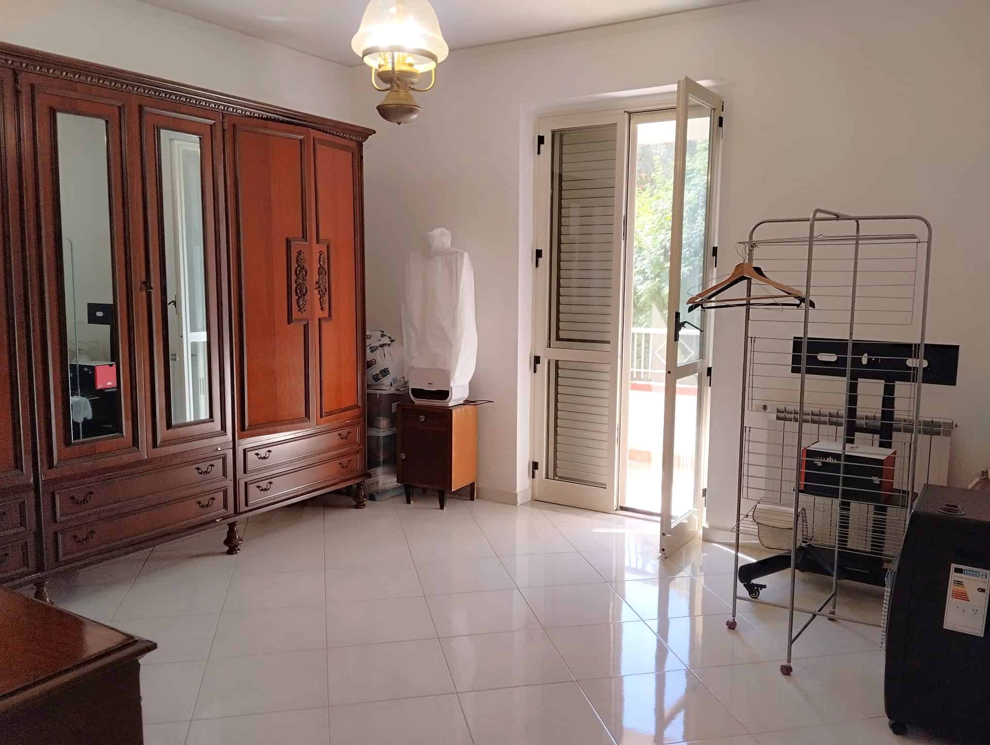 Interno di un appartamento con armadio in legno, porta finestra e scaffale metallico, ambiente luminoso e spazioso.