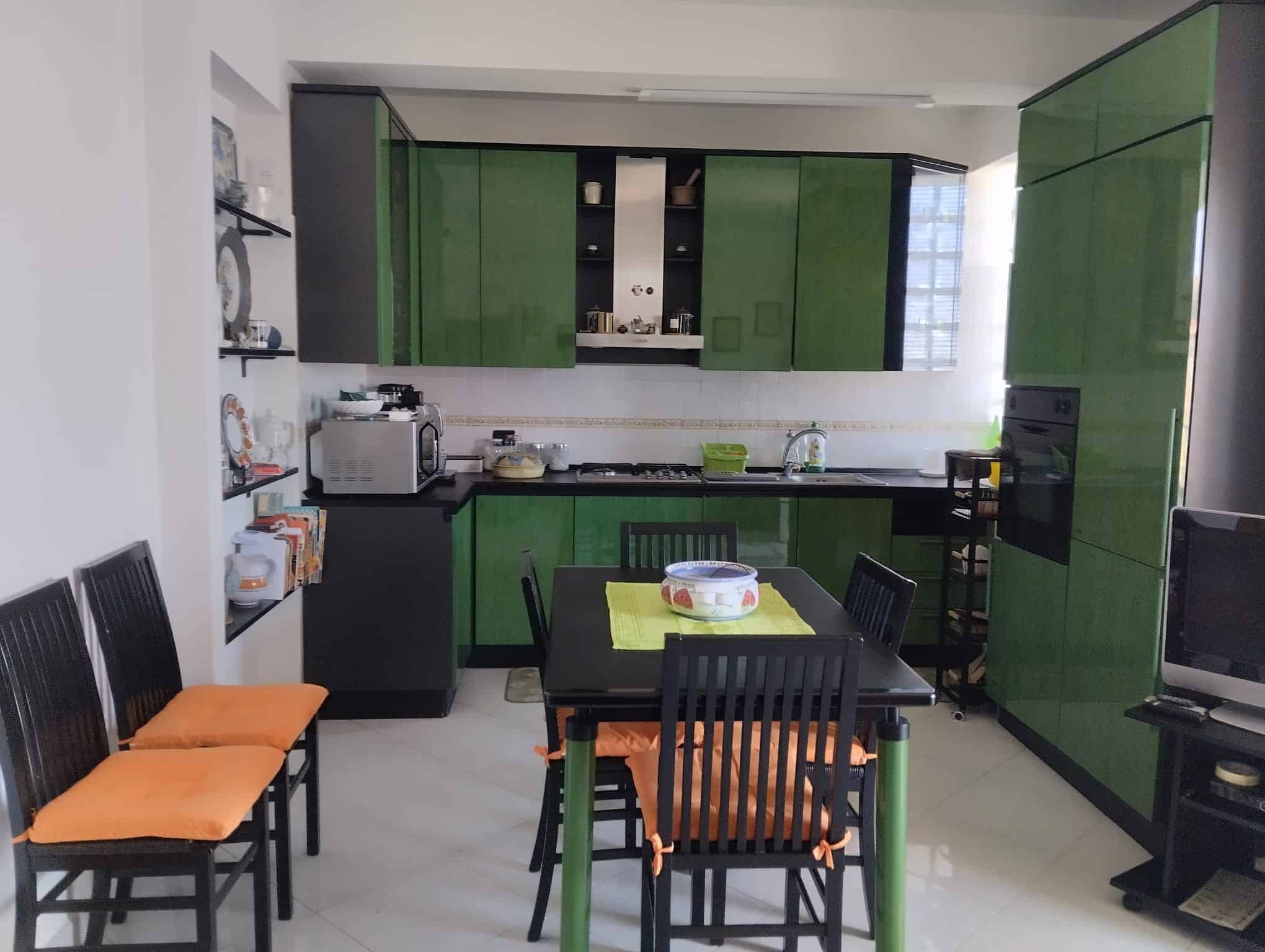 Cucina moderna con mobili verdi e zona pranzo con tavolo e sedie nere in un appartamento in vendita a Acquedolci, Me.