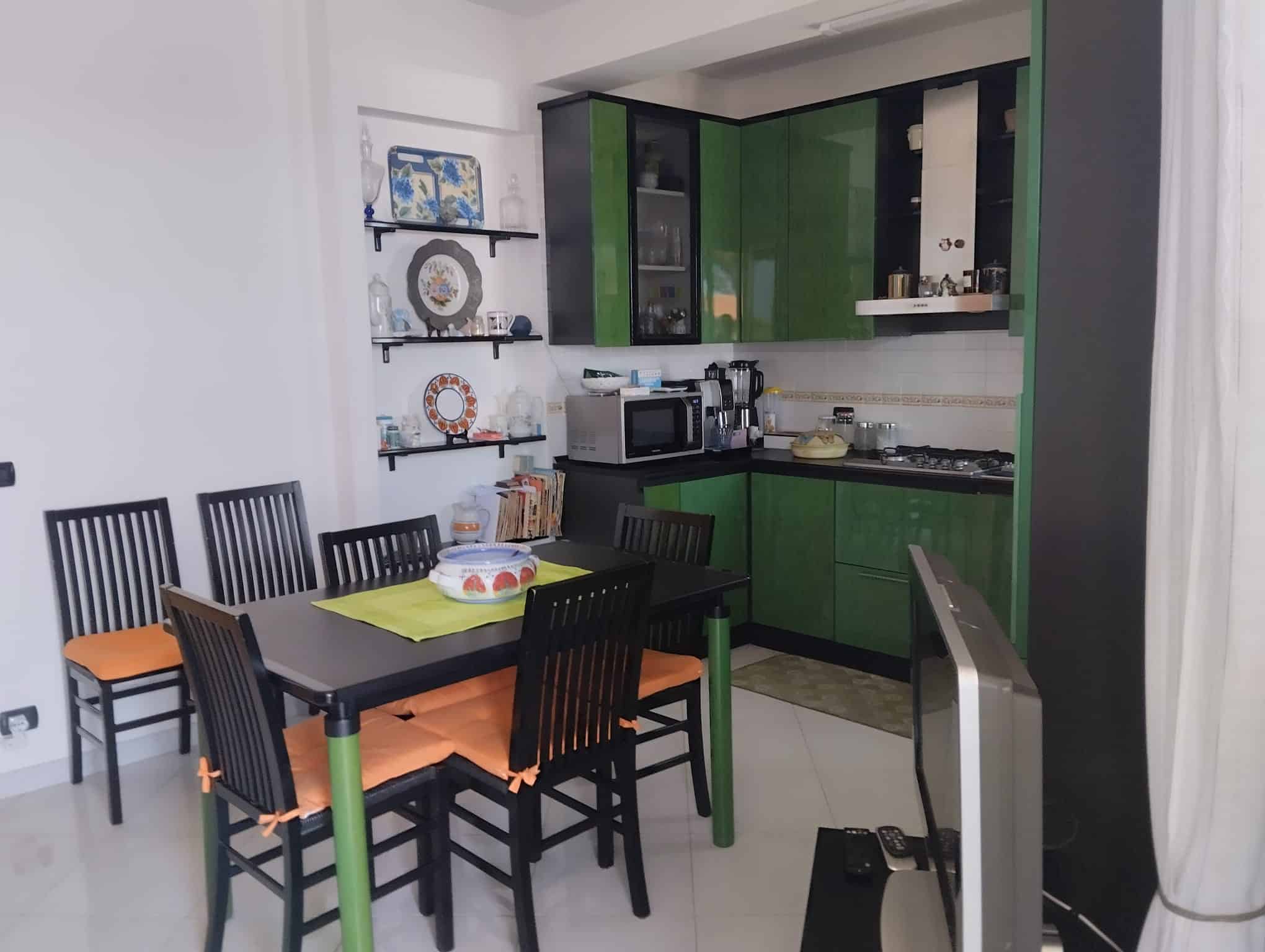 Cucina moderna in appartamento in vendita a Acquedolci, con mobili verdi e nero, tavolo con sedie nere e cucina attrezzata.