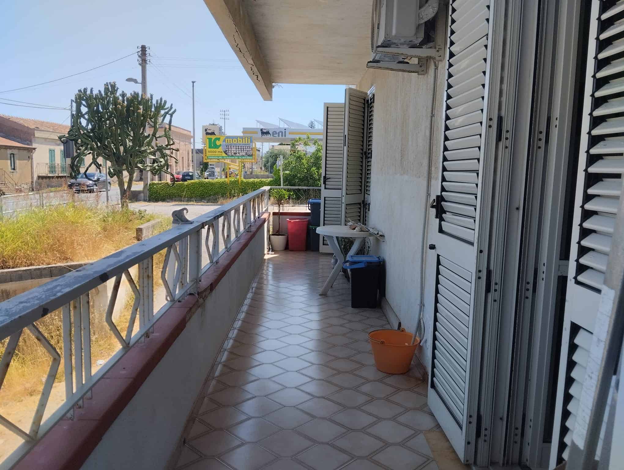 Balcone di un appartamento con vista sulla strada e su alcune case e negozi in lontananza.