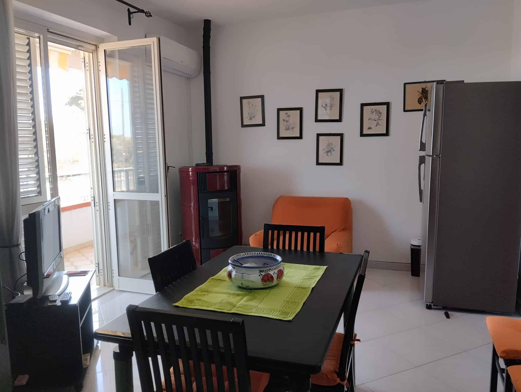 Interno di un appartamento con tavolo da pranzo, balcone e pareti decorate con quadri.