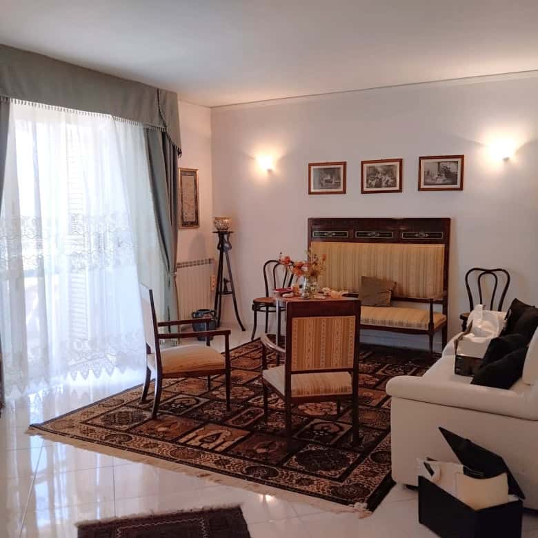 Interno di un appartamento in vendita con soggiorno arredato, divani, sedie e decorazioni classiche.