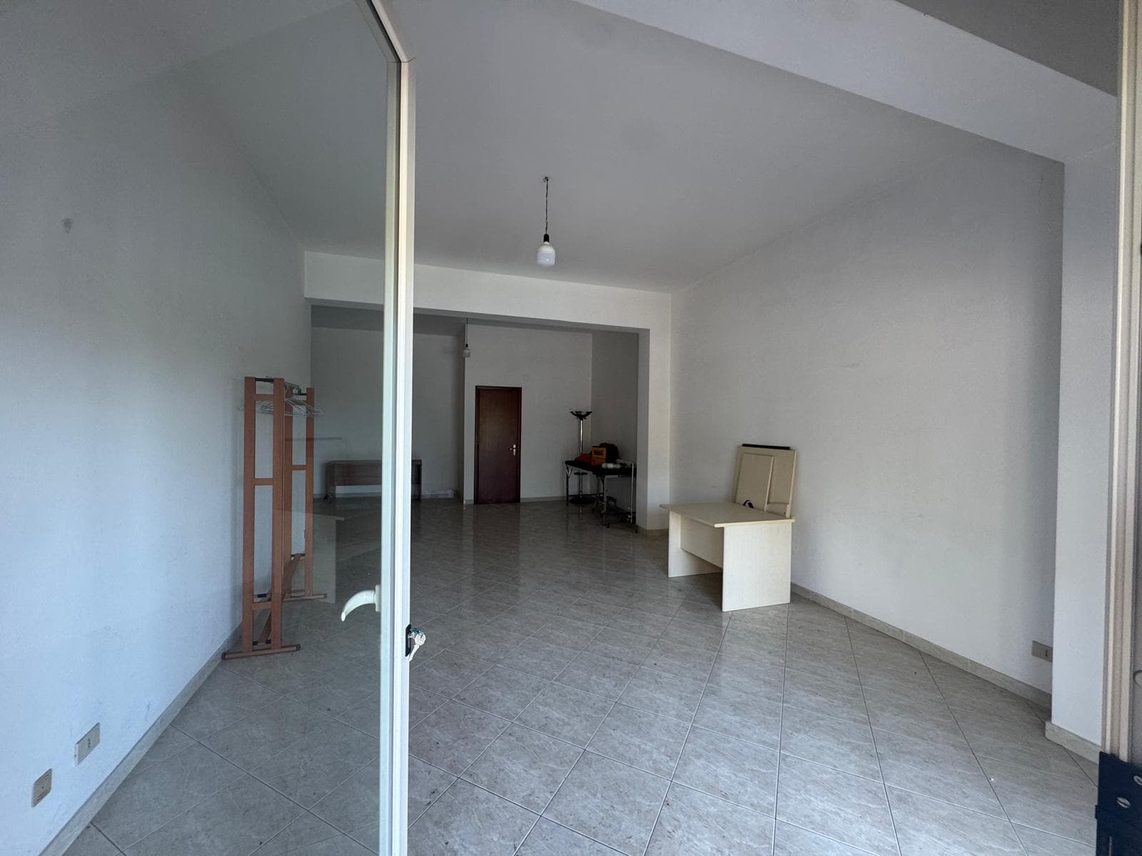 Interno di un appartamento vuoto con pareti bianche e pavimento in piastrelle, spazio luminoso e arioso.