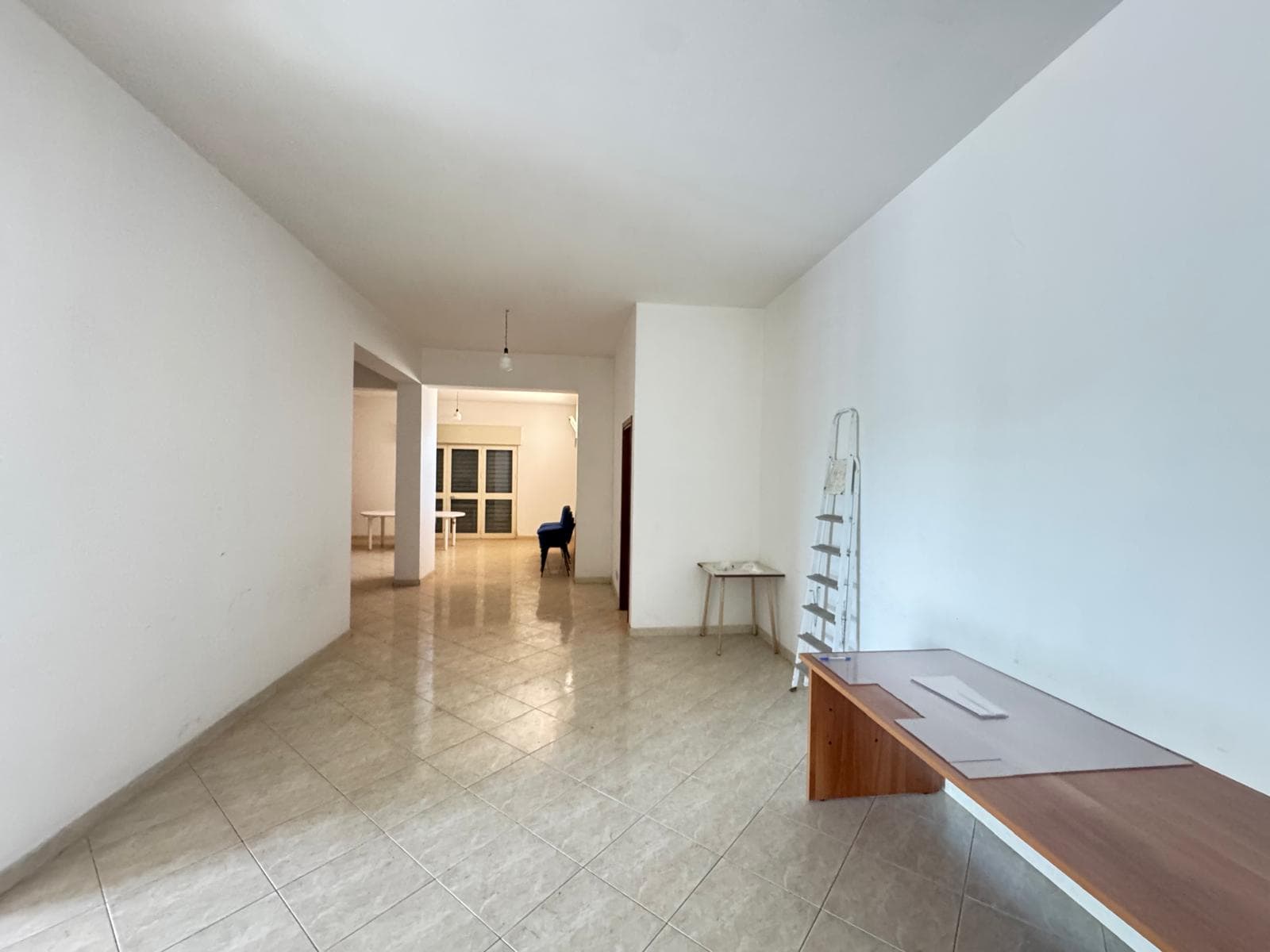 Interno di un appartamento vuoto con pareti bianche e pavimento in piastrelle beige, spazio luminoso e spazioso.