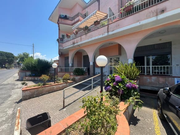 Edificio residenziale con balconi e giardino fiorito, vista esterna in una giornata soleggiata.