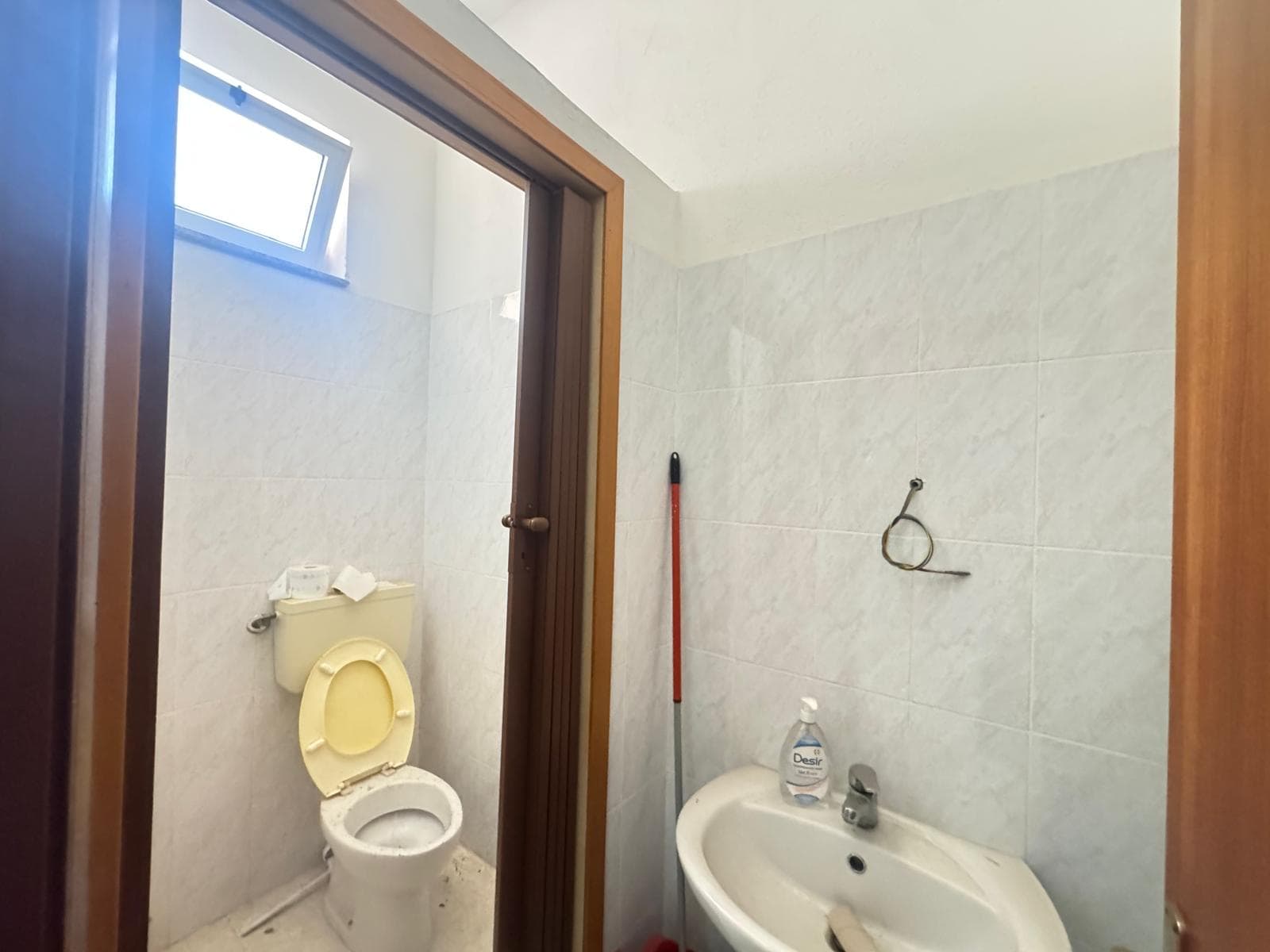 Bagno di piccole dimensioni con WC e lavabo, finestra per ventilazione naturale, pareti rivestite in piastrelle chiare, ambiente luminoso e funzionale.
