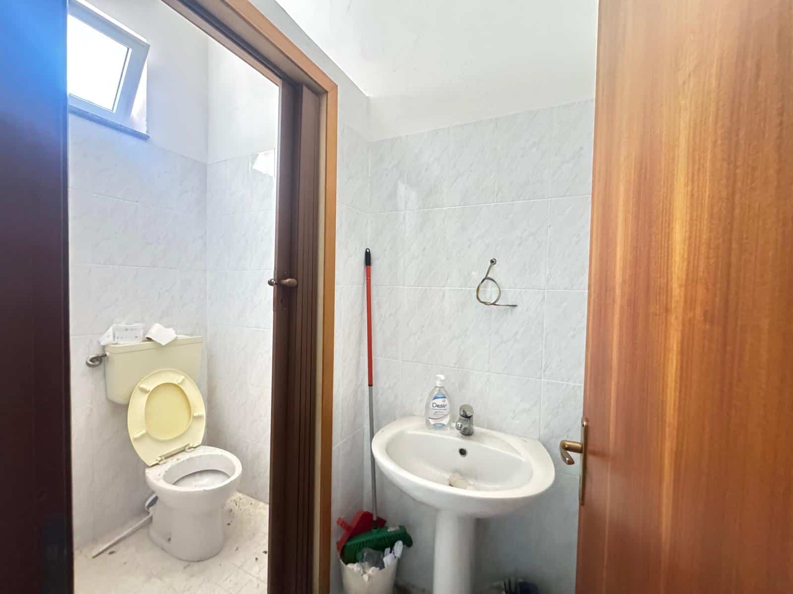 Bagno con WC e lavabo in una casa NextCasa, con pareti in piastrelle bianche e finestra alta per illuminazione naturale.