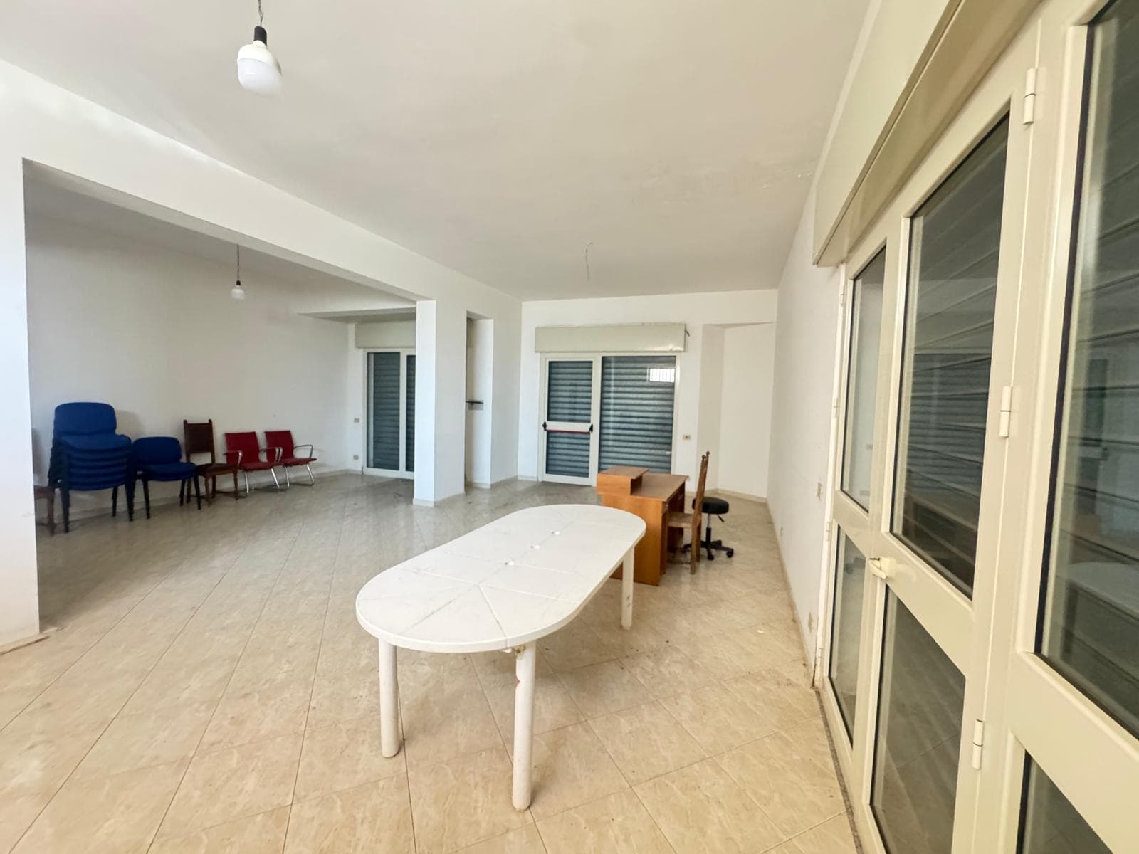 Ampio spazio interno di un appartamento con pareti bianche, grandi finestre e mobili di base, ideale per affitti a breve termine o residenze.