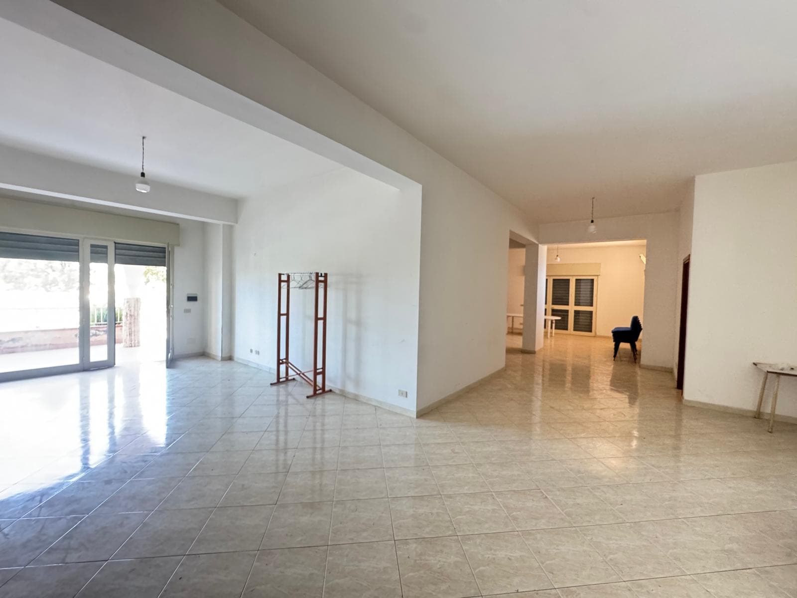 Interno di un appartamento vuoto con grandi finestre e pavimento in piastrelle, pronto per essere arredato.