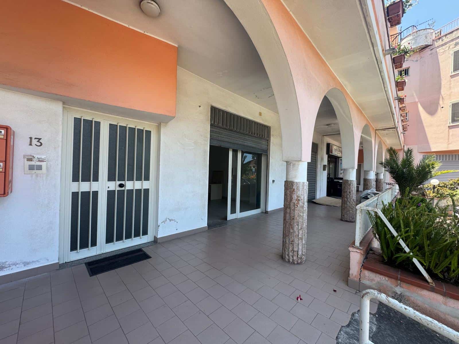 Facciata di un edificio residenziale con portico e colonne, ingresso con porta scorrevole e piante ornamentali, in zona urbana.
