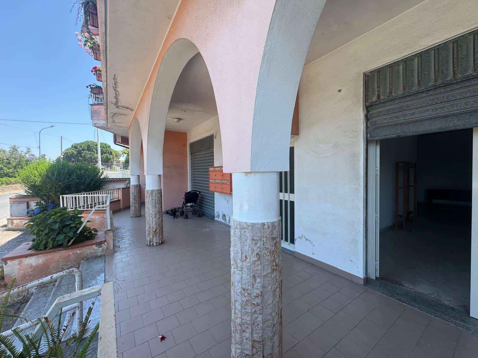 Facciata di un edificio residenziale con archi e colonne, ingresso con garage e balcone con fiori, in una zona tranquilla e ben curata.