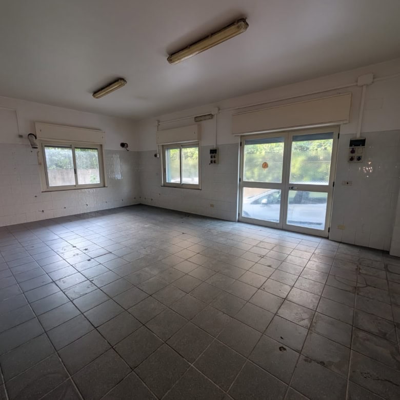 Locale commerciale vu dall'interno con grandi finestre e pavimento in piastrelle, pronto per ristrutturazione.