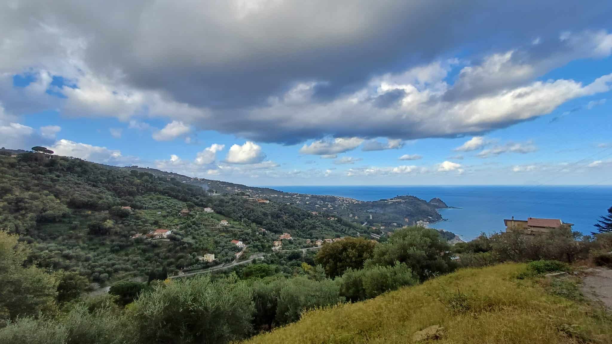 Paesaggio costiero con colline verdi, cielo nuvoloso e vista sul mare in Sicilia.