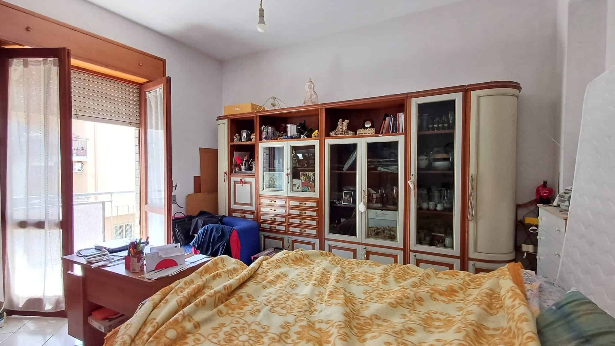 Camera da letto luminosa con armadio in legno e balcone con vista sulla strada.