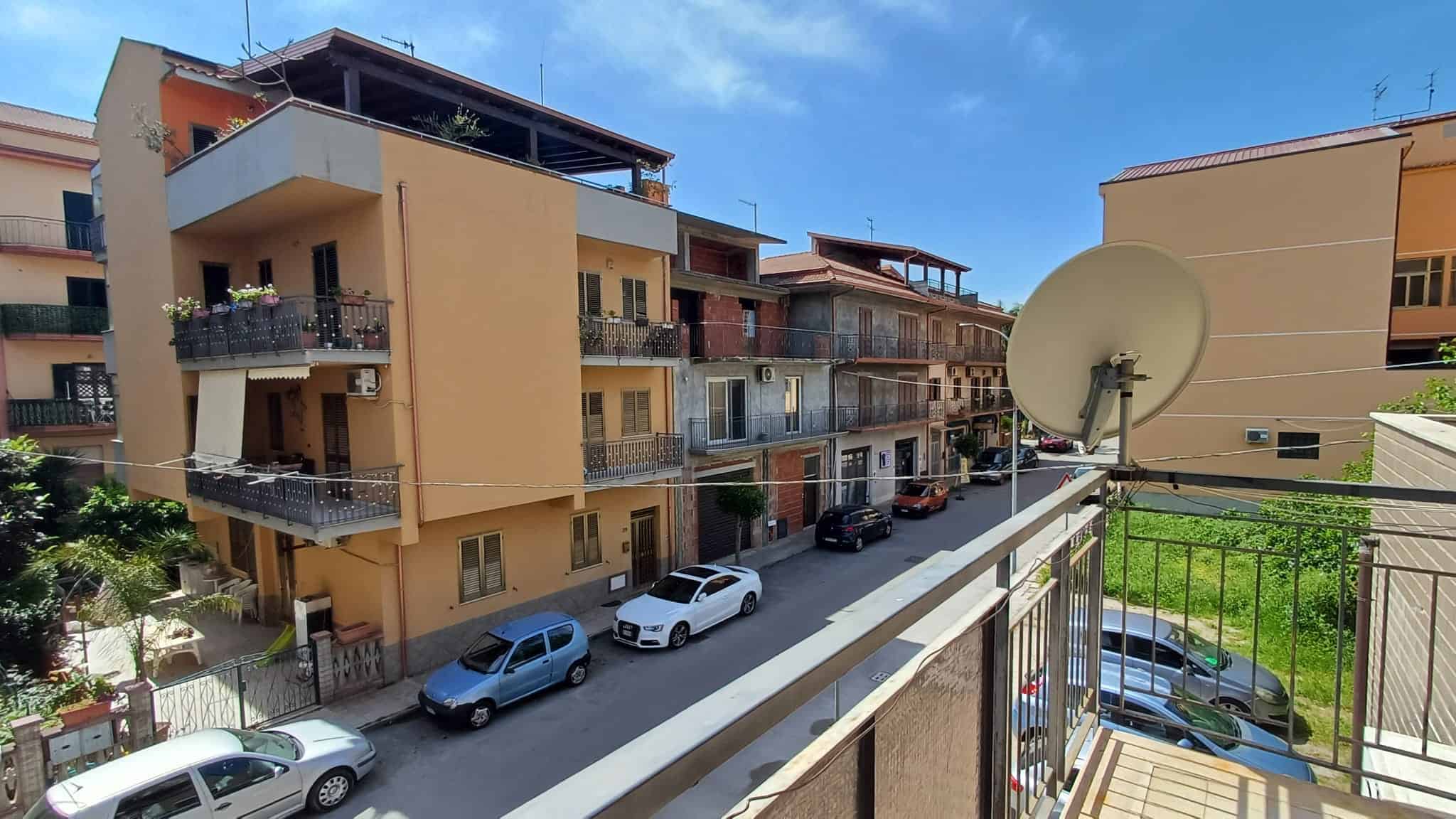 Vista di un complesso residenziale con balconi e auto parcheggiate in strada, in zona urbana.
