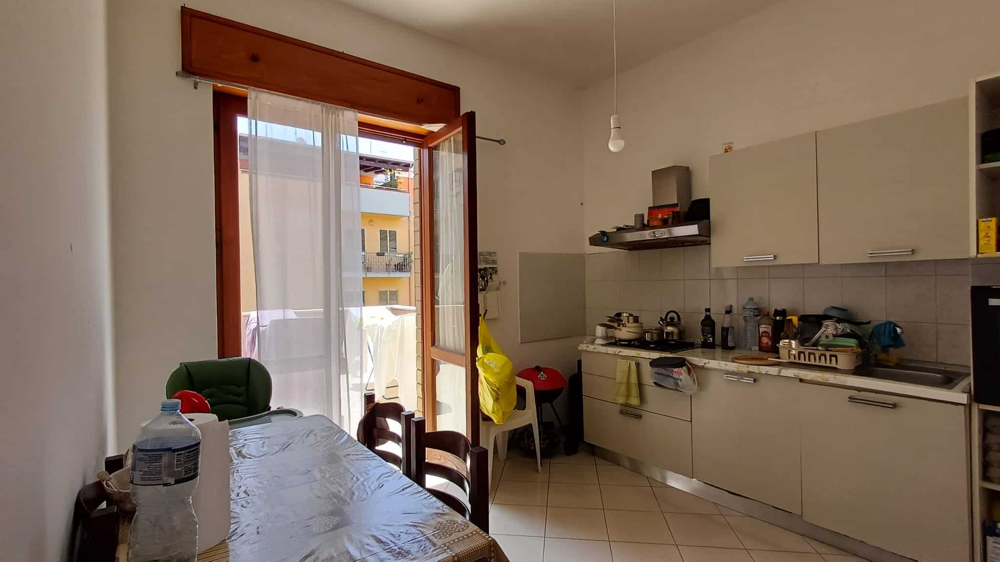 Cucina moderna con accesso a balcone, mobili bianchi e elettrodomestici, ambiente luminoso e funzionale.