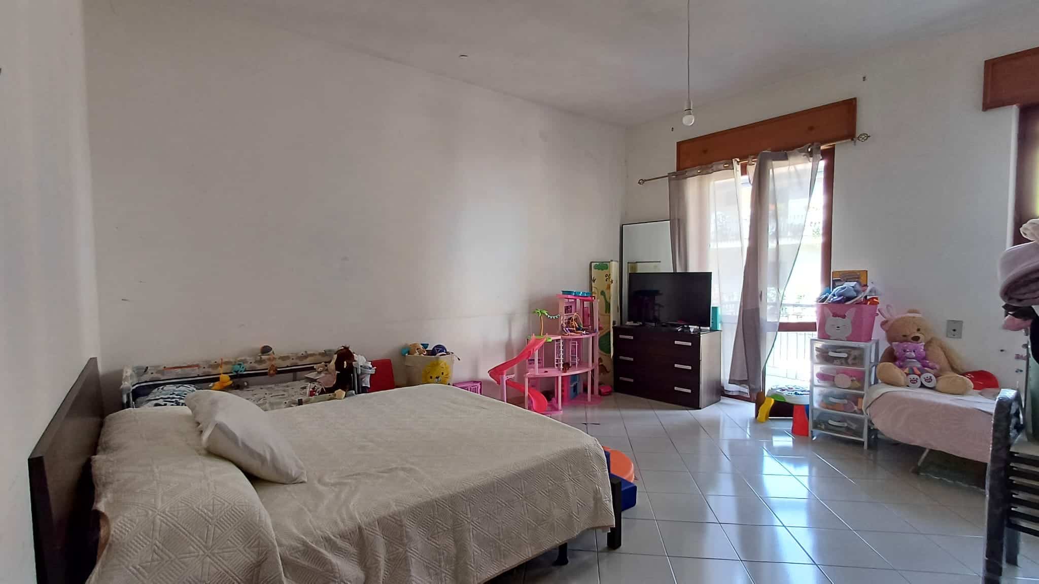 Camera che mostra una camera da letto con letto matrimoniale, giochi per bambini, e mobili vari in una casa a Rocca di Capri Leone.
