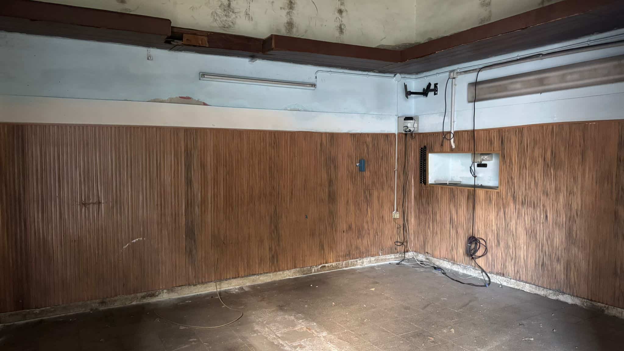 Magazzino vuoto in fase di ristrutturazione, con pareti in legno e pavimento in cemento, pronto per essere trasformato in uno spazio funzionale e moderno.
