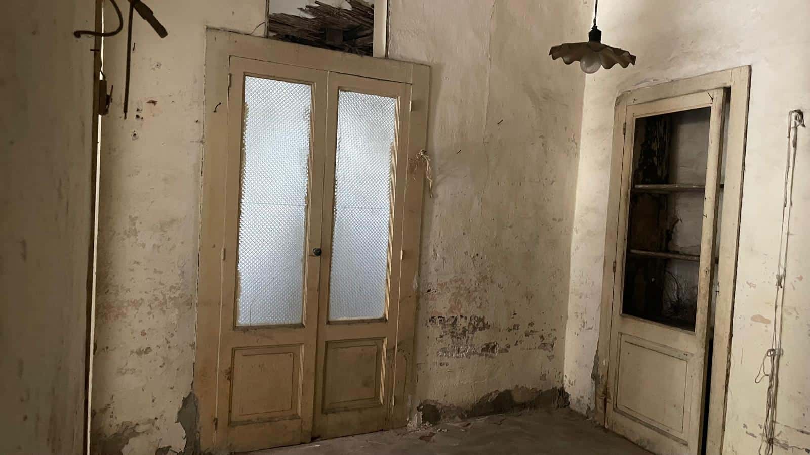 Immagine di un interno di casa in stile rustico con porte in legno vecchie e pareti con segni di usura, creando un'atmosfera autentica e vintage.