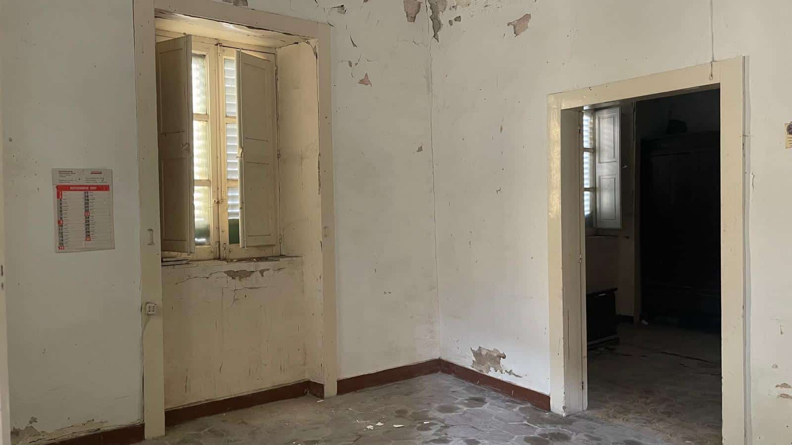 Ambiente interno di una casa da ristrutturare con pareti danneggiate e finestre con persiane, pronto per lavori di rinnovamento e miglioramento.