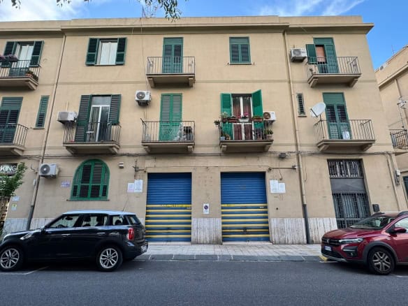 Edificio residenziale con garage e balconi, situato in zona urbana, con auto parcheggiate davanti.