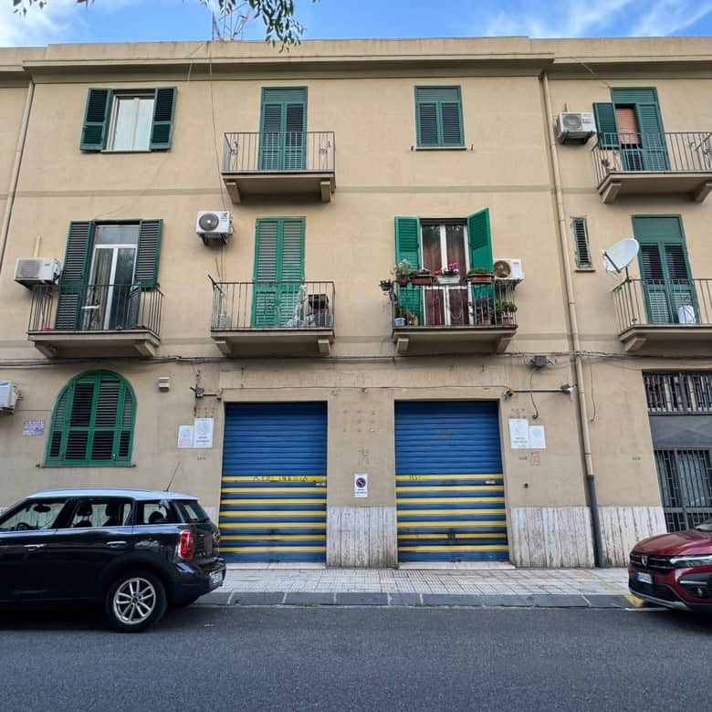 Edificio residenziale con garage e balconi, situato in zona urbana, con auto parcheggiate davanti.