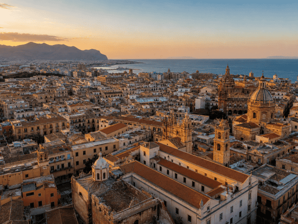 Panoramica di Palermo con il mare e le montagne sullo sfondo al tramonto, evidenziando l'architettura storica e il paesaggio urbano.