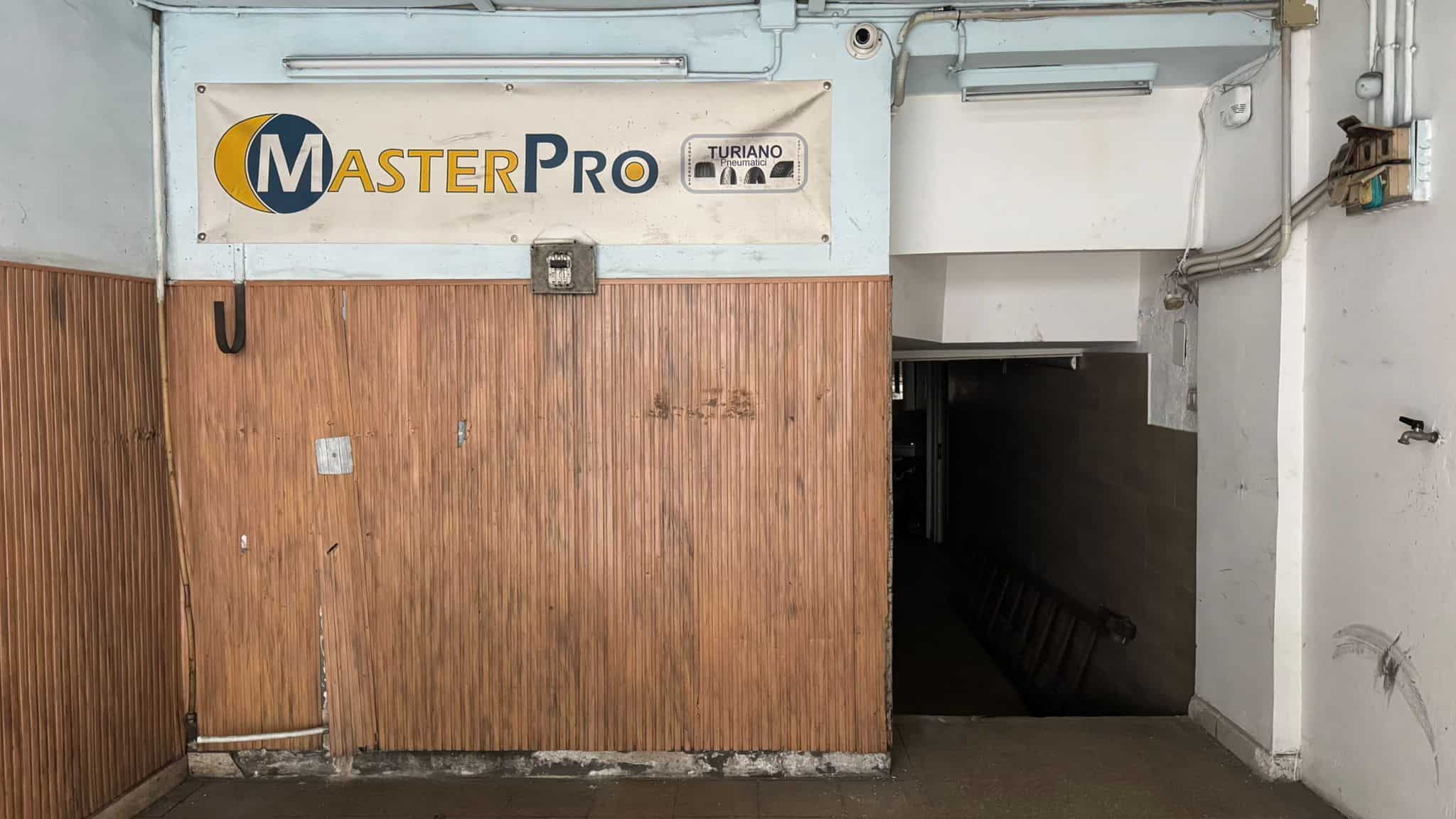 Spazio di magazzino con ingresso in garage, pareti in legno e accesso tramite porta scorrevole, ideale per deposito o uso commerciale.