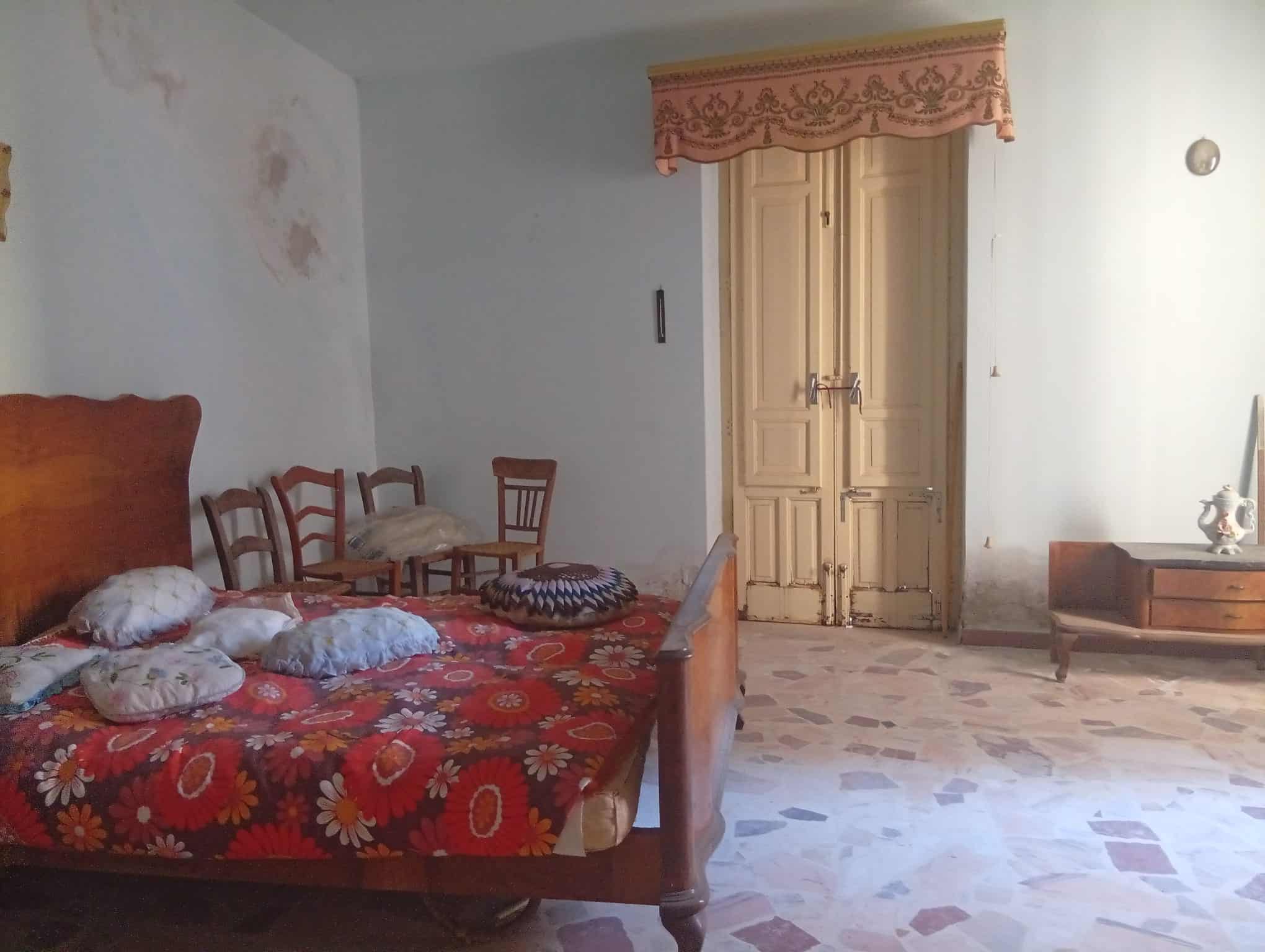 Interno di una camera da letto con letto matrimoniale, sedie e armadio in una casa in vendita a Ficarra, Messina.