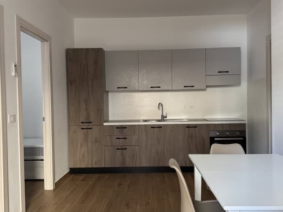 Cucina moderna con mobili in legno chiaro, pareti bianche e piano di lavoro in laminato, dotata di lavello e armadietti superiori e inferiori, ambiente luminoso e funzionale.