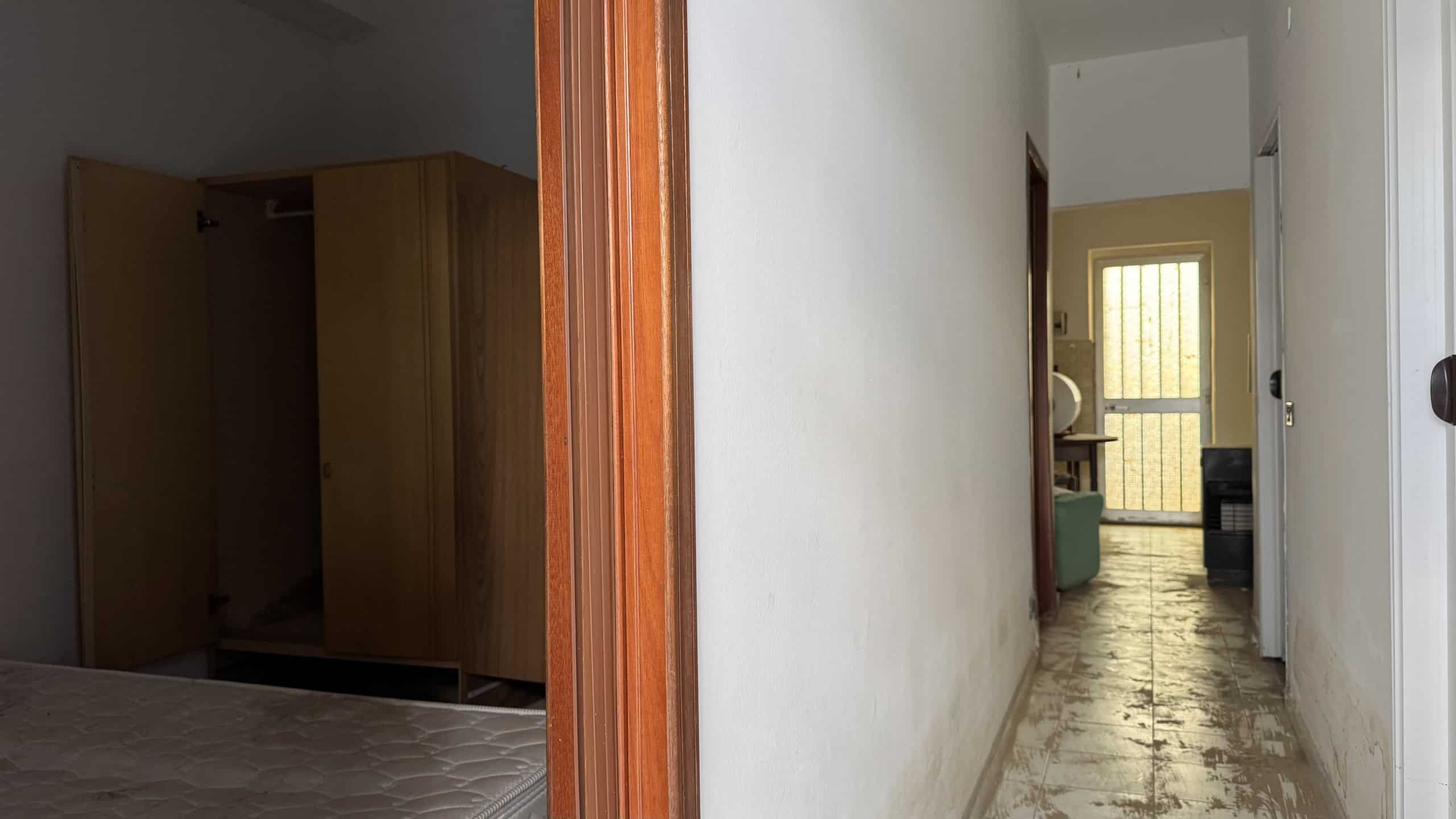 Armadio a muro in legno in una stanza da letto, vista da una porta aperta, con pareti bianche e pavimento in piastrelle.
