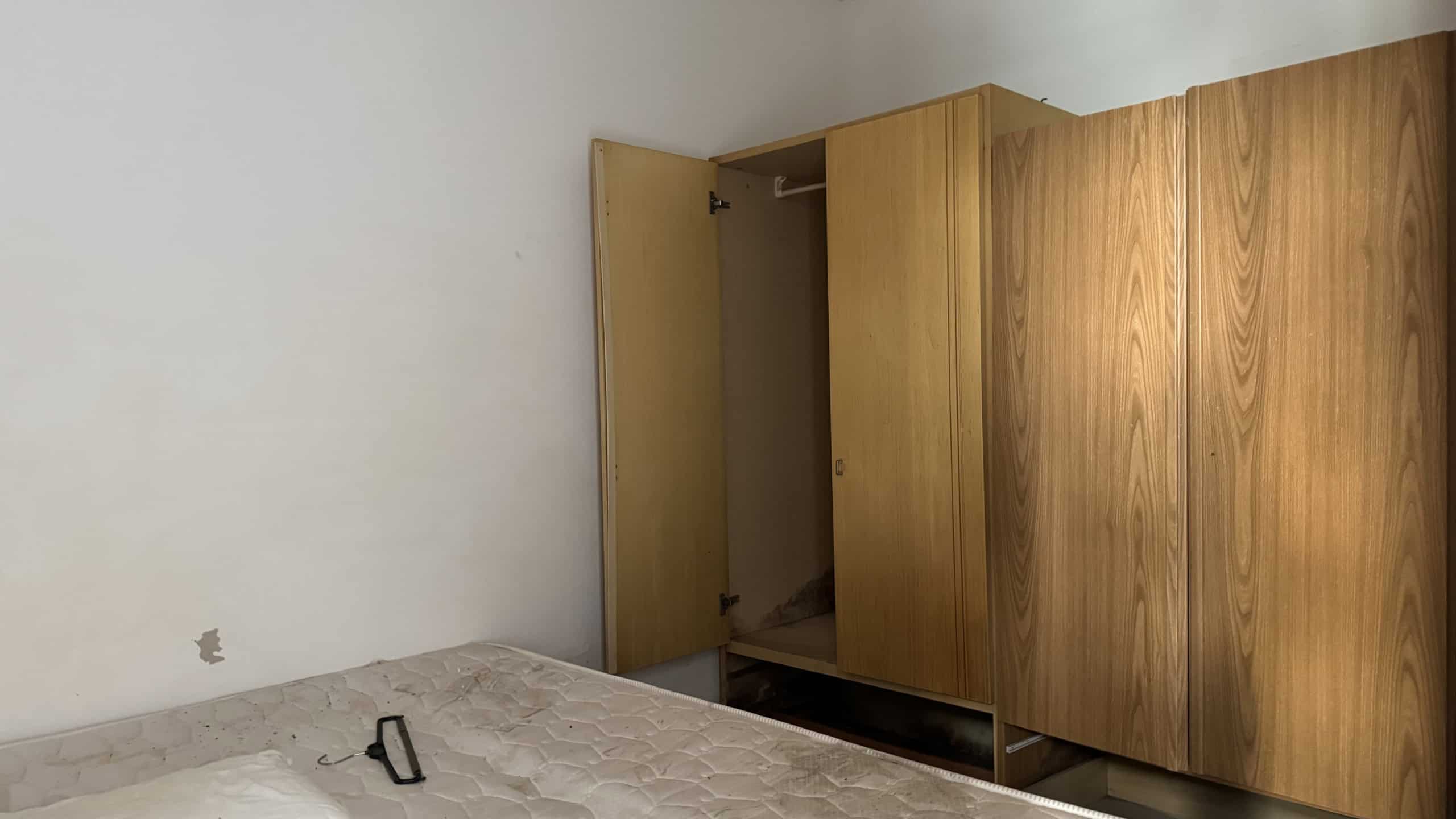 Armadio in legno con ante scorrevoli in una camera da letto moderna. Spazio interno visibile con ripiani e appendiabiti, ambiente luminoso e minimalista. Ideale per arredamento funzionale e di design.