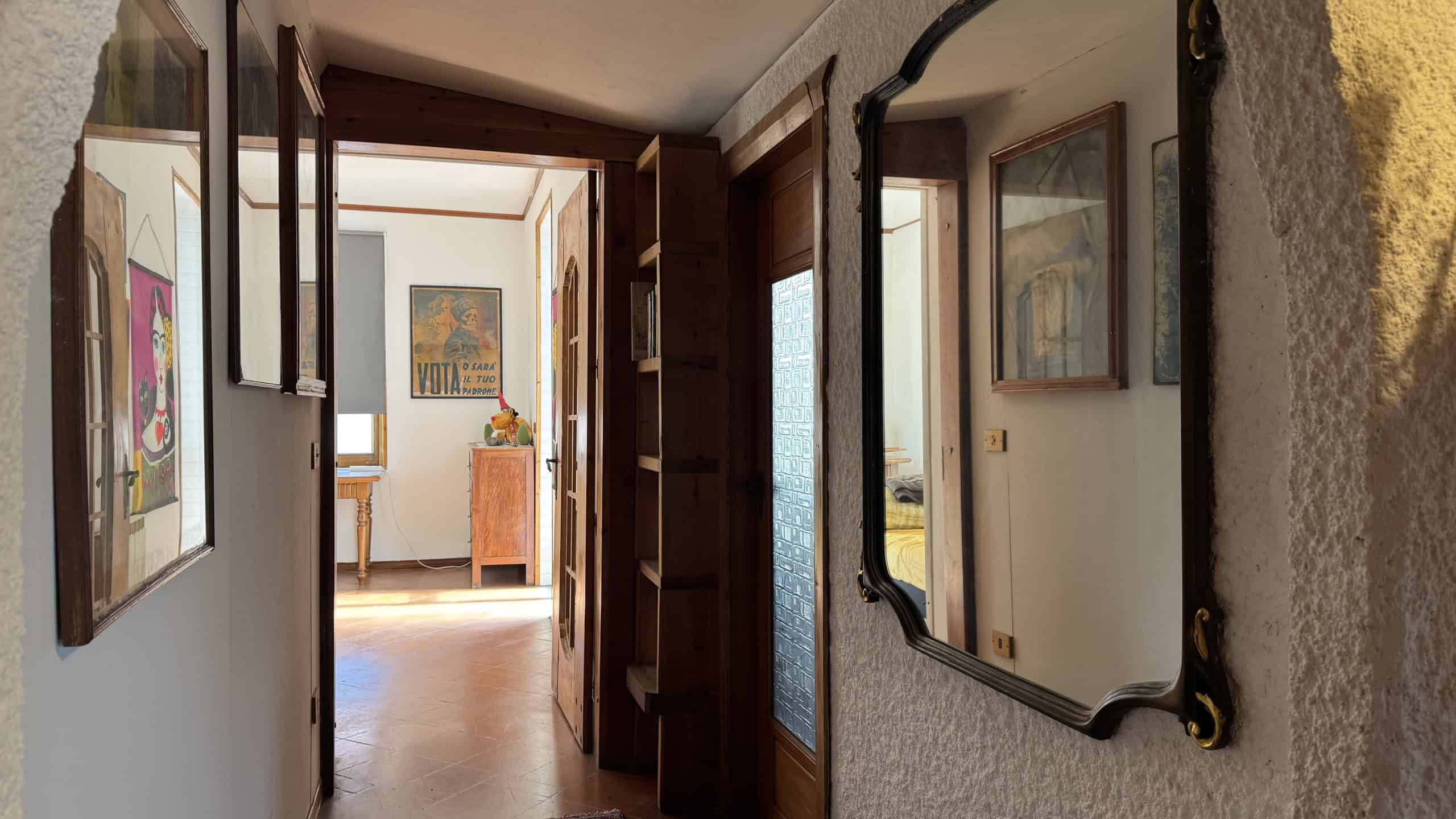 Ampio ingresso con pareti decorate da quadri e grande specchio antico, illuminato dalla luce naturale che entra dalle finestre, creando un ambiente accogliente e elegante.